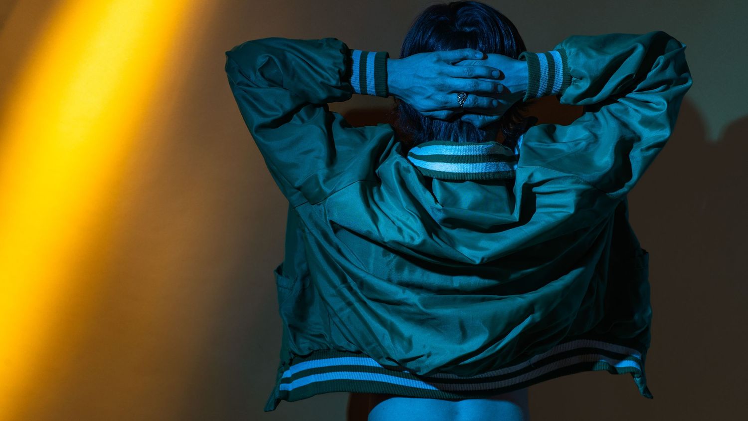 Silhouette of person wearing hoodie against blue and yellow lighting effects.