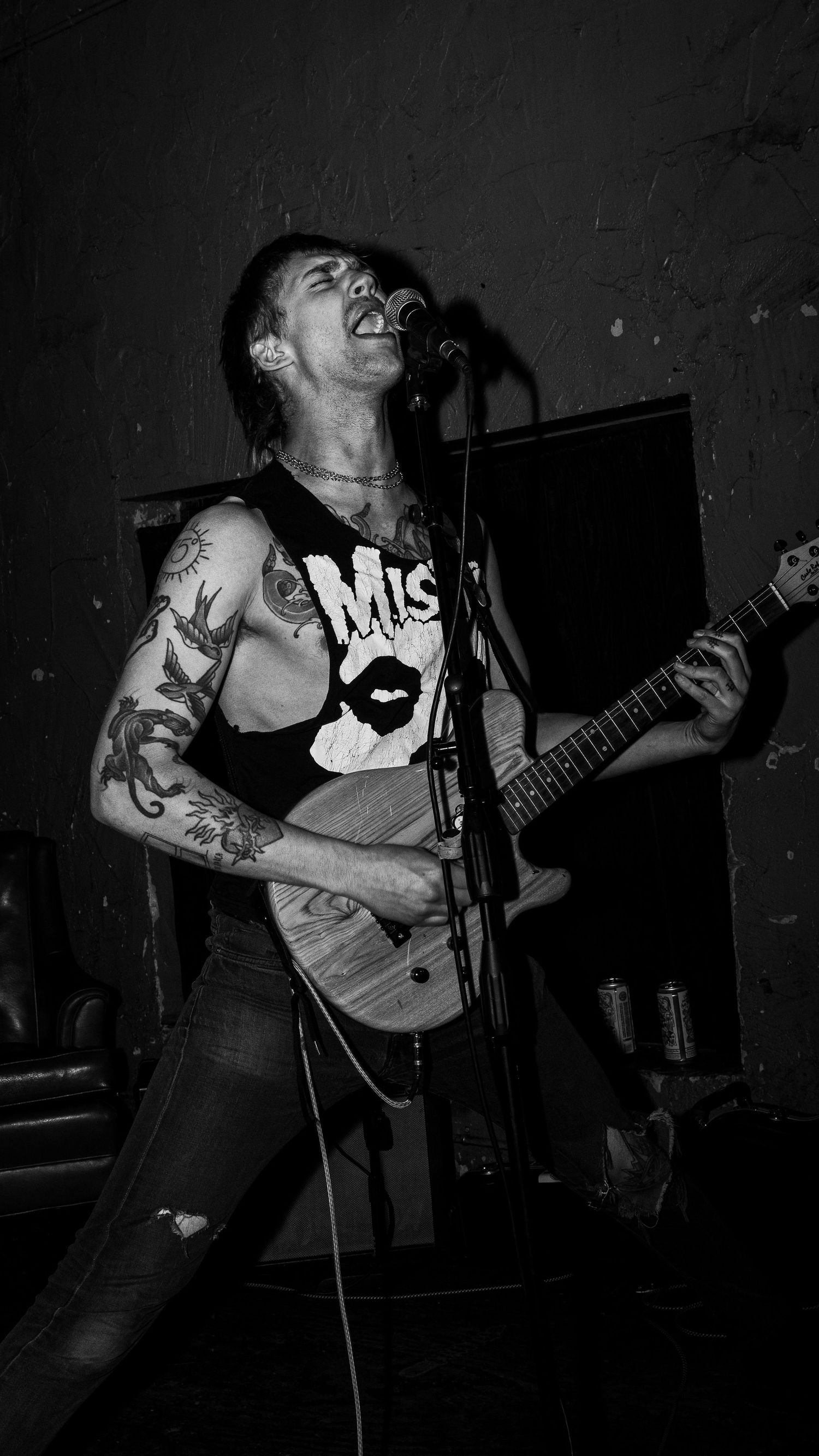 Energetic punk rock performer with tattoos playing guitar on stage in black and white.