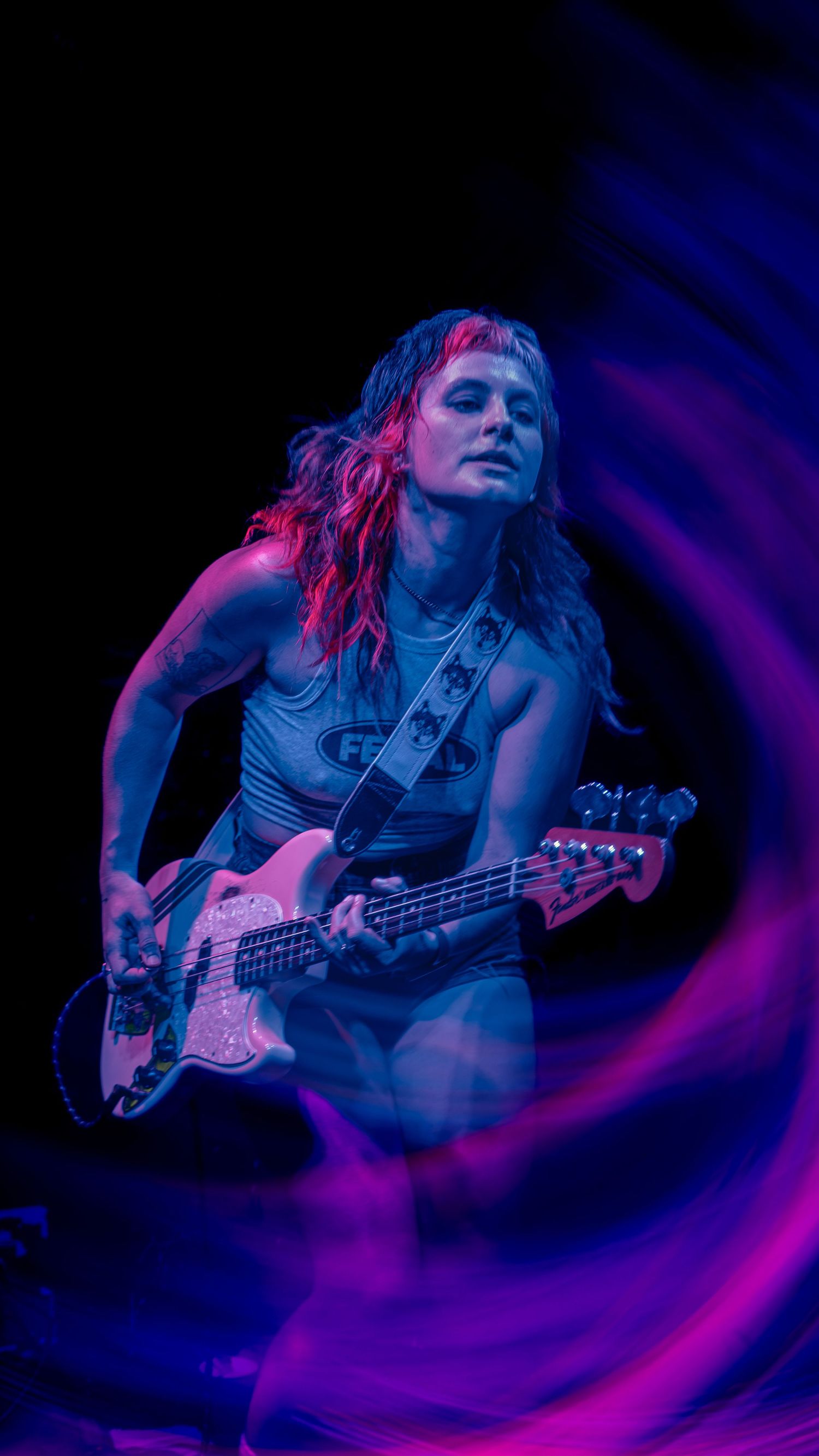 Bass guitarist performing on stage illuminated by vibrant blue and purple lighting during a concert performance.