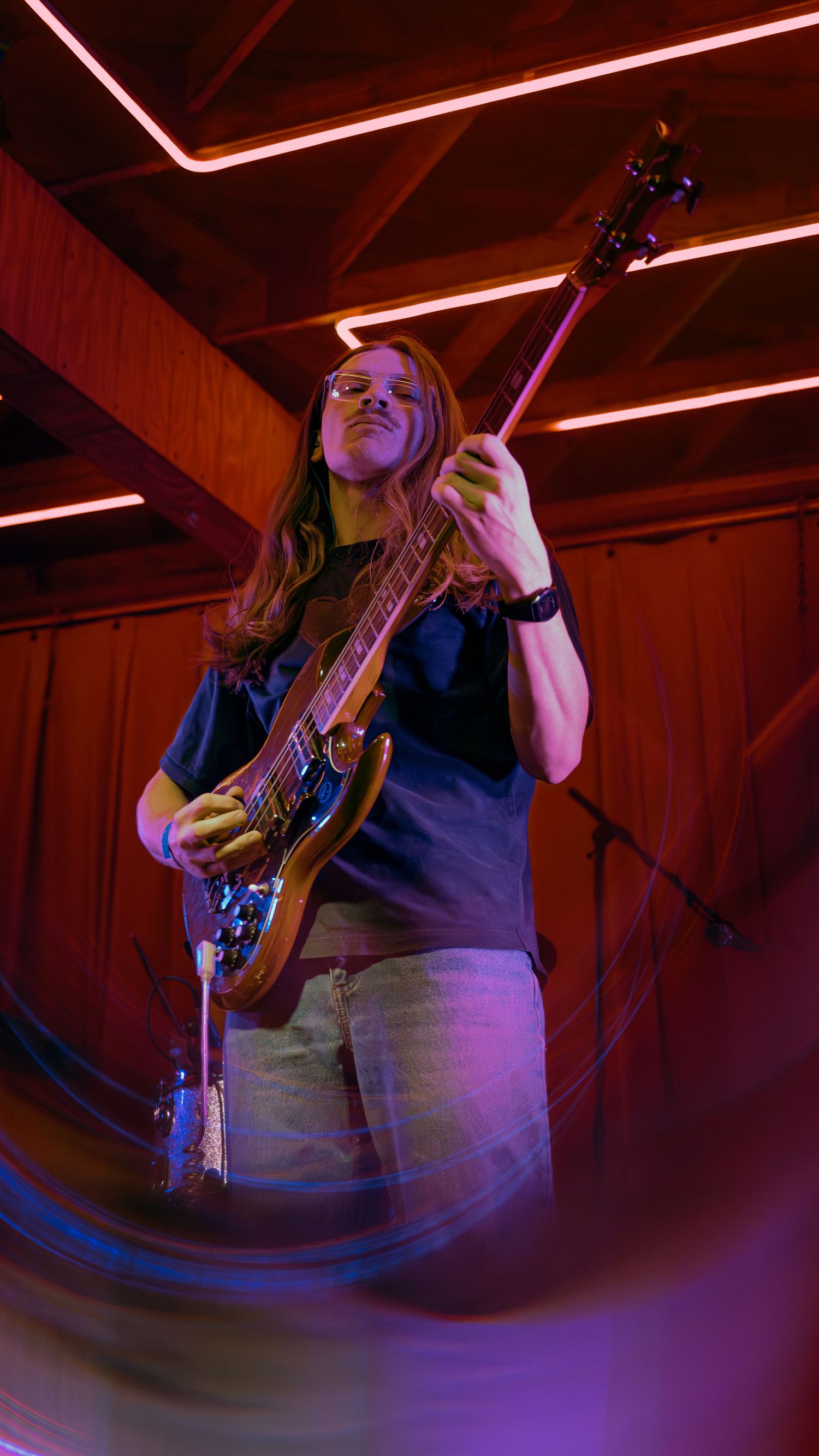 Guitarist performing on stage with motion blur effects under dramatic red and blue lighting.