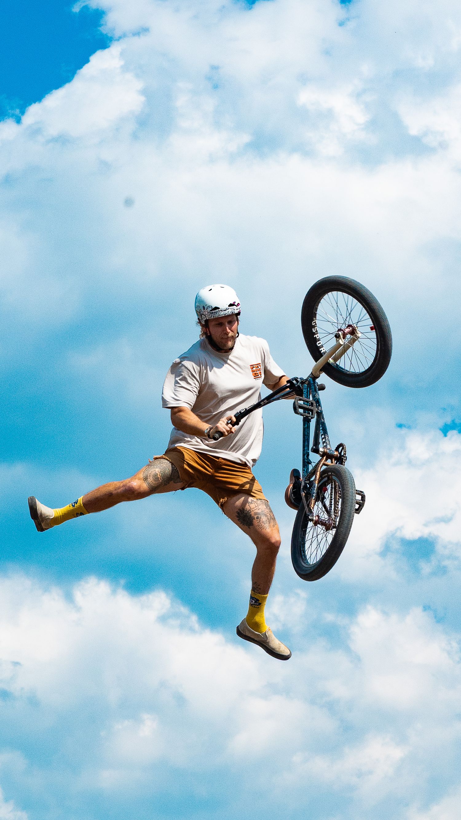 BMX rider in yellow shoes performs dynamic bike trick against blue sky.