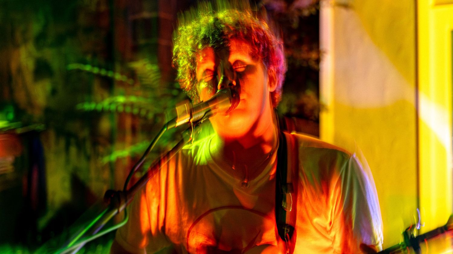 Concert performer singing on stage with colorful motion blur effects in yellow and orange lighting.