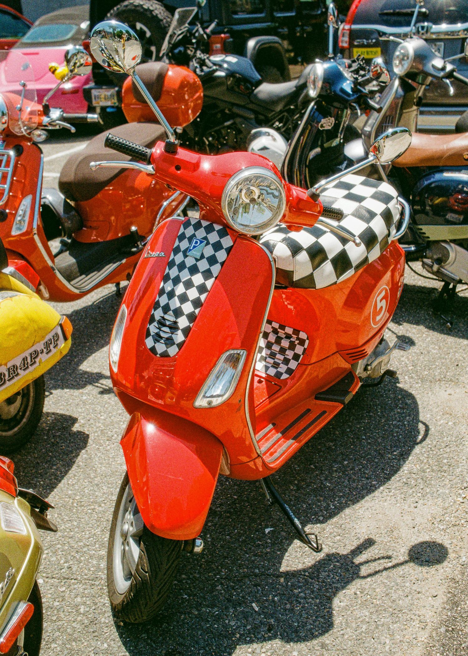 Red Vespa scooters with checkered racing flags lined up at an outdoor motorcycle show or event.