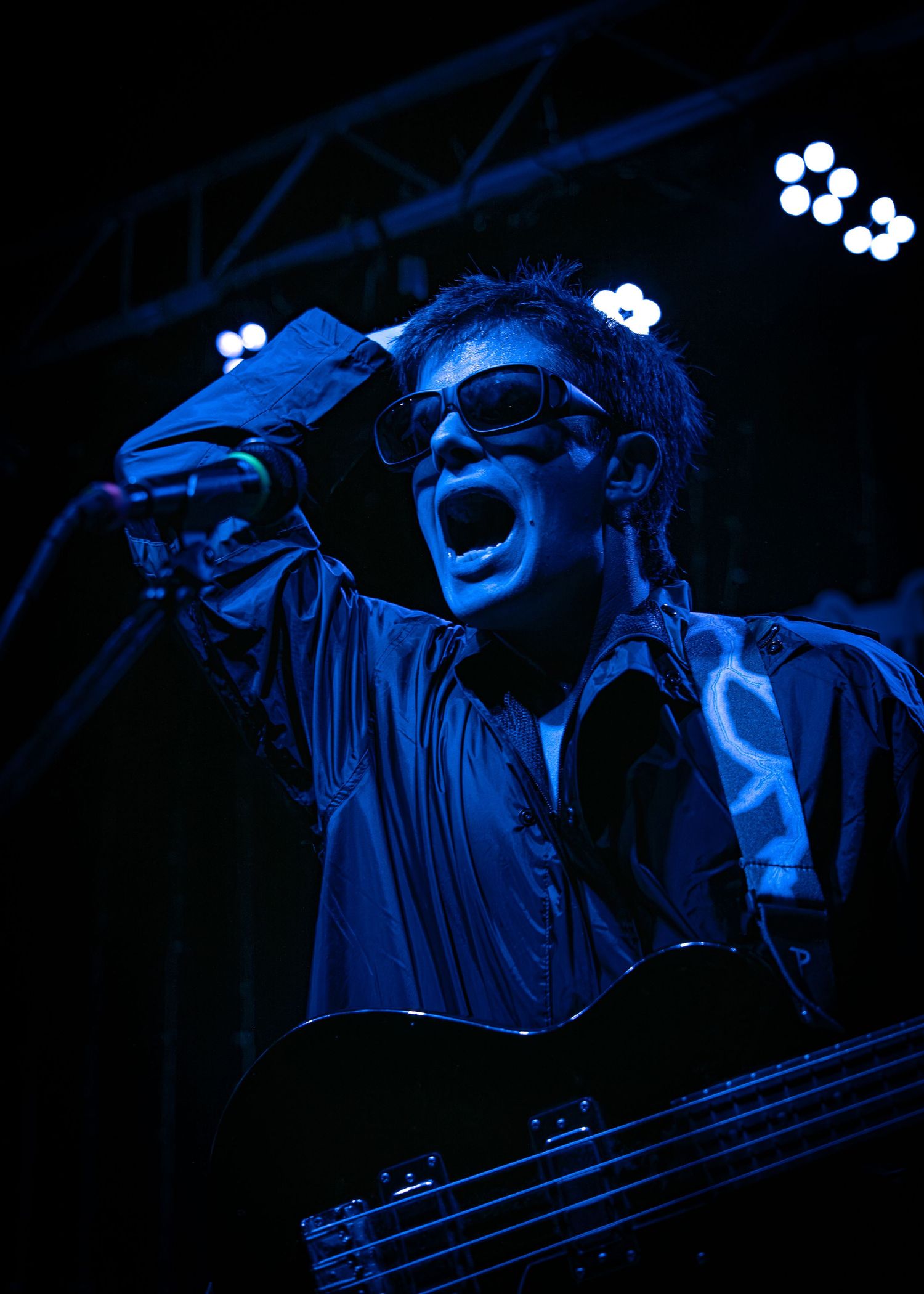 A performer in dramatic lighting gestures passionately during what appears to be an opera or theatrical performance.