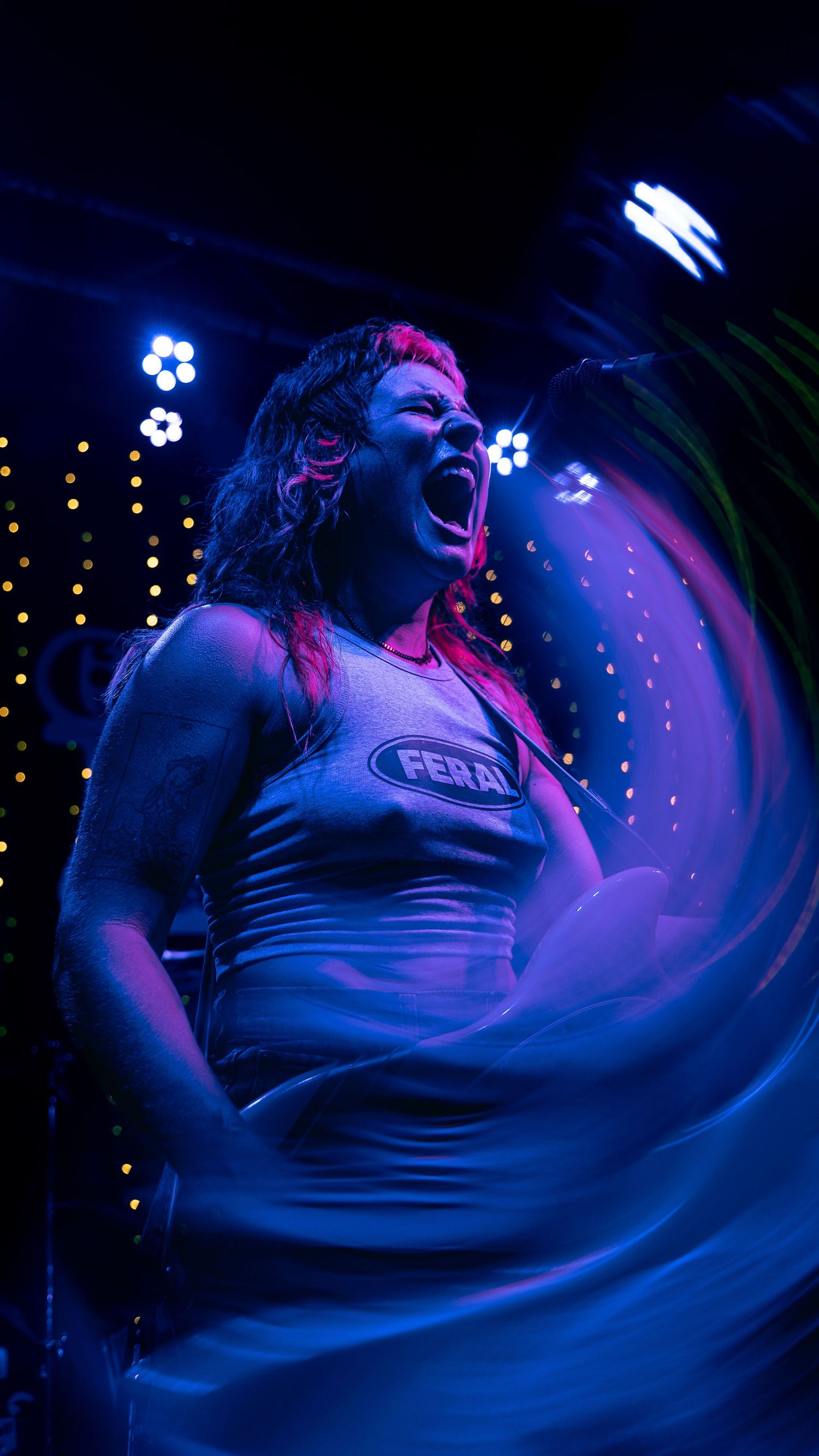 A performer sings passionately on stage illuminated by dramatic blue and purple lighting.