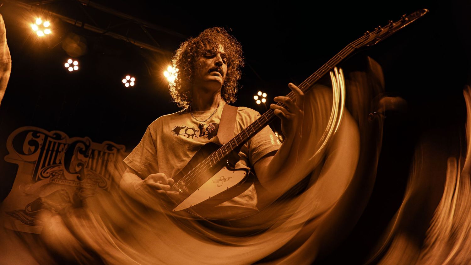 An energetic guitarist performs on stage under warm lighting, creating a dramatic motion blur effect during a live performance.
