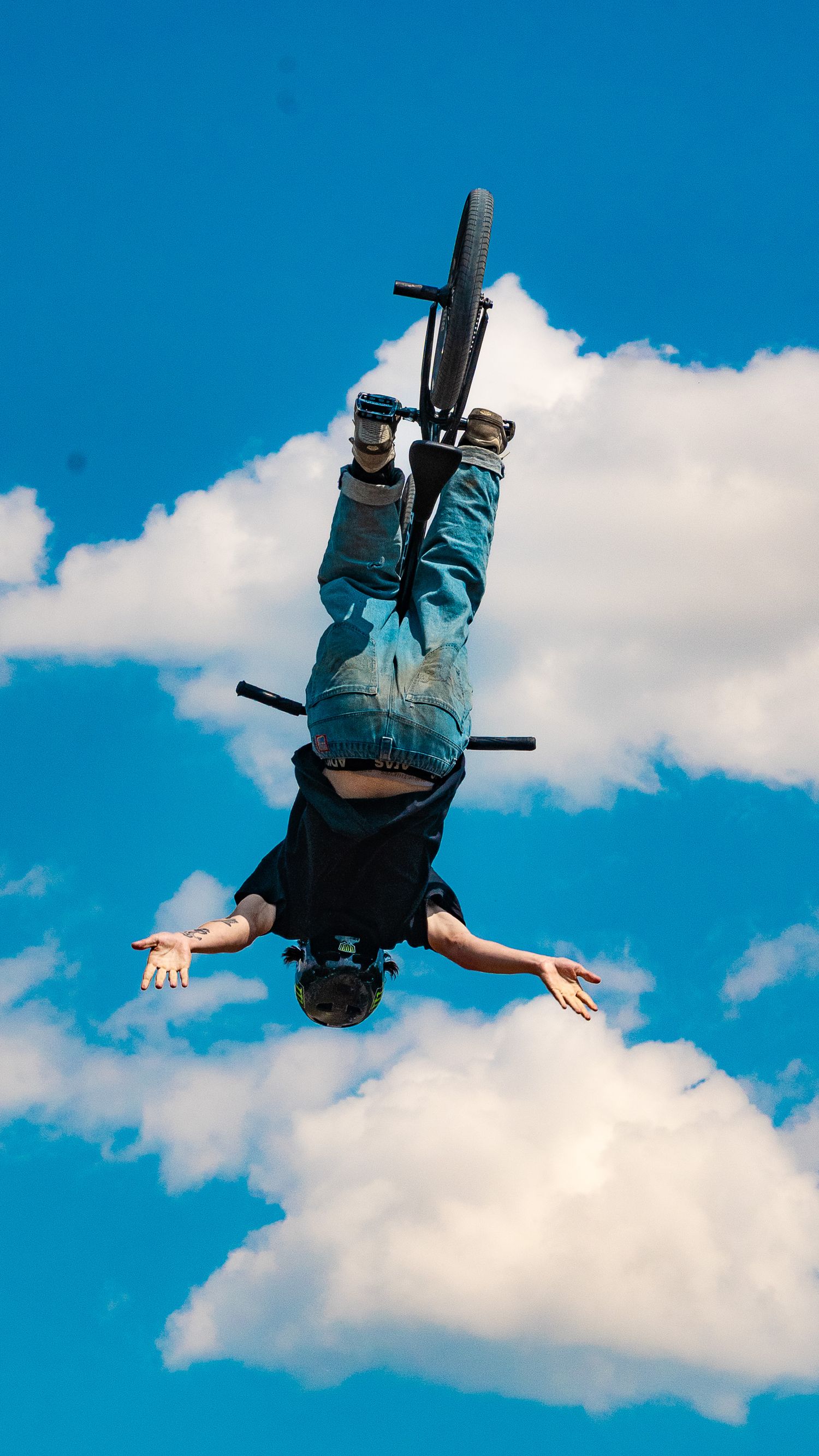 BMX rider executes inverted aerial trick with bike above clouds.
