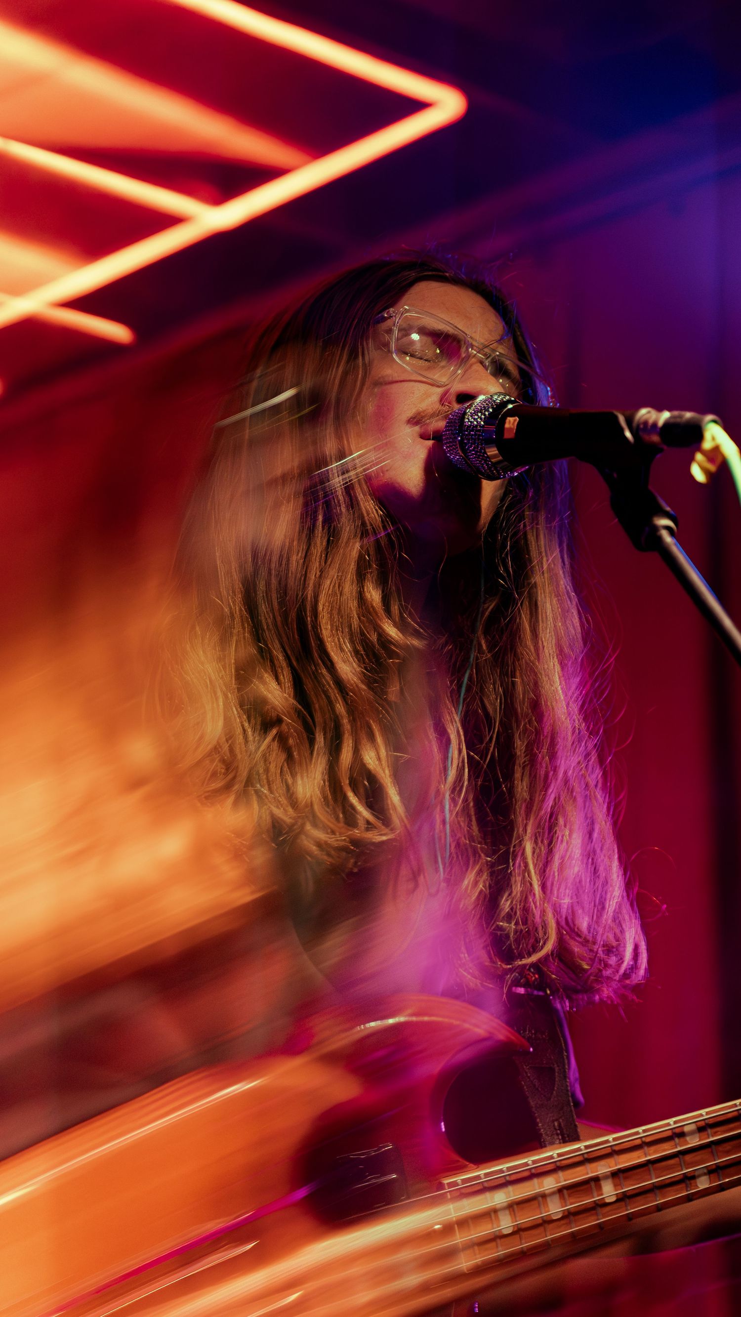 A performer sings on stage with dramatic red and purple lighting creating an atmospheric concert environment.
