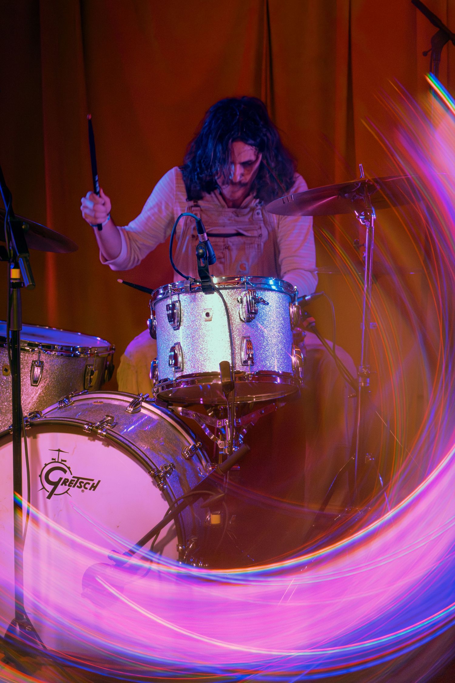Drummer performs at venue with dynamic light trails creating pink and blue streaks across a moody stage.