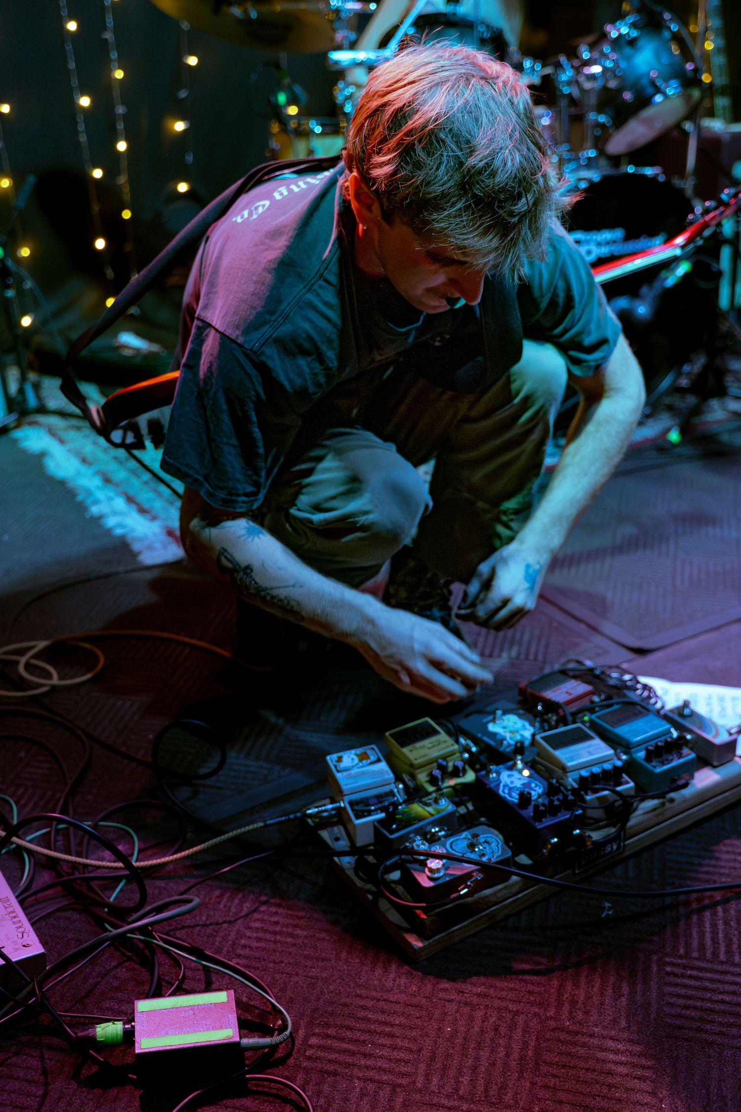 Close-up shot of hands operating electronic music equipment and effect pedals in dim concert lighting.