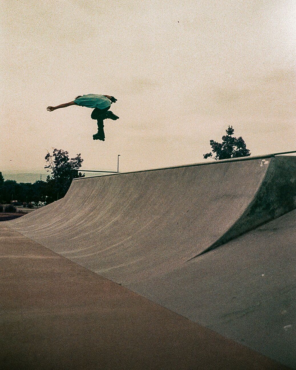 A skater executes an aerial maneuver on a concrete halfpipe against a dusky sky.