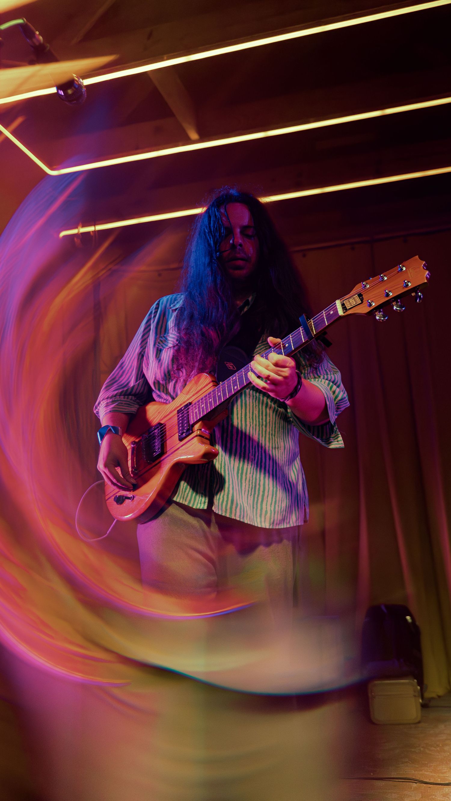 Musician playing acoustic guitar on stage with vibrant swirling purple and yellow light trails creating dynamic motion effects.