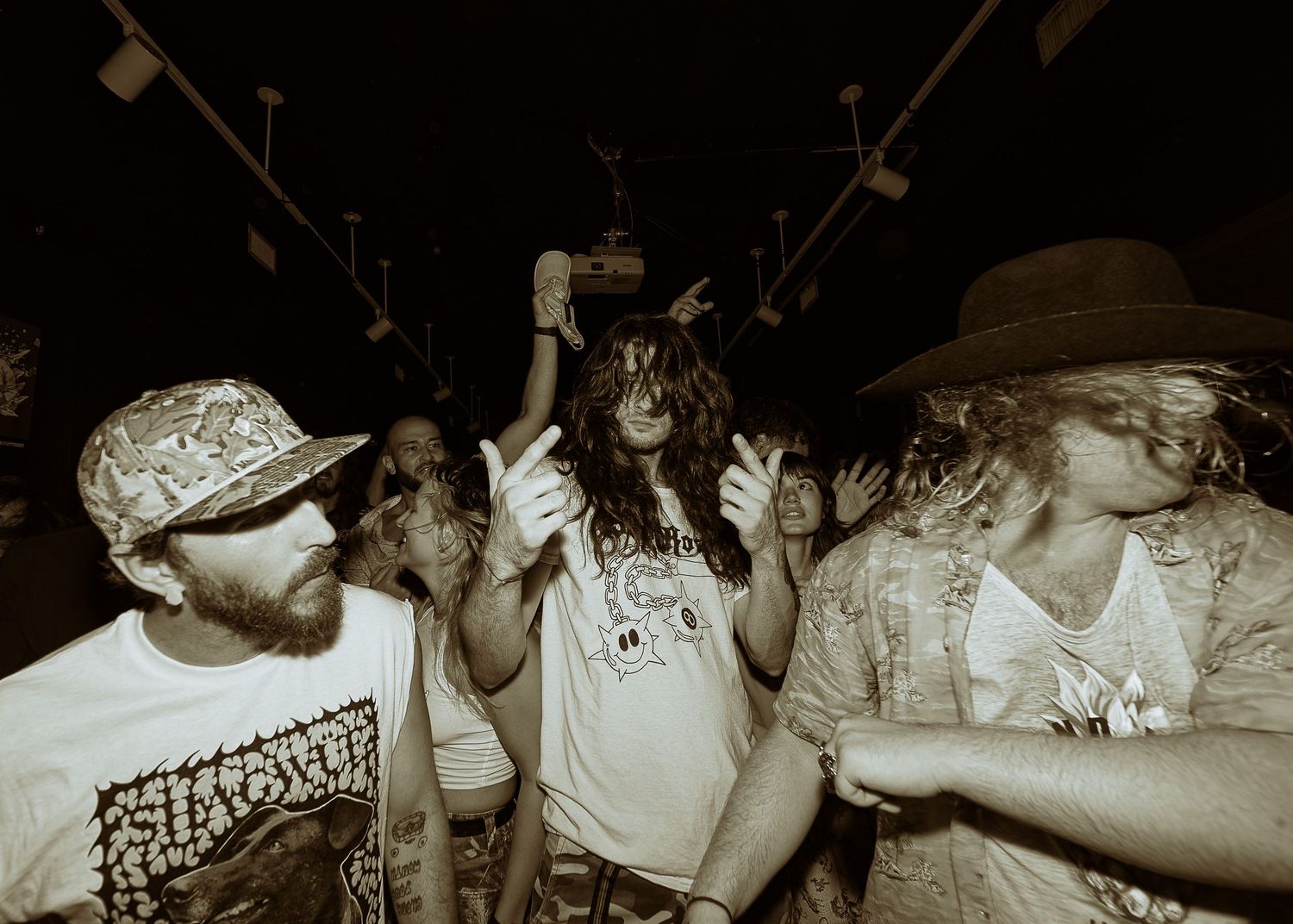 An energetic crowd in a sepia-toned photograph dances and parties at what appears to be a concert or club event.