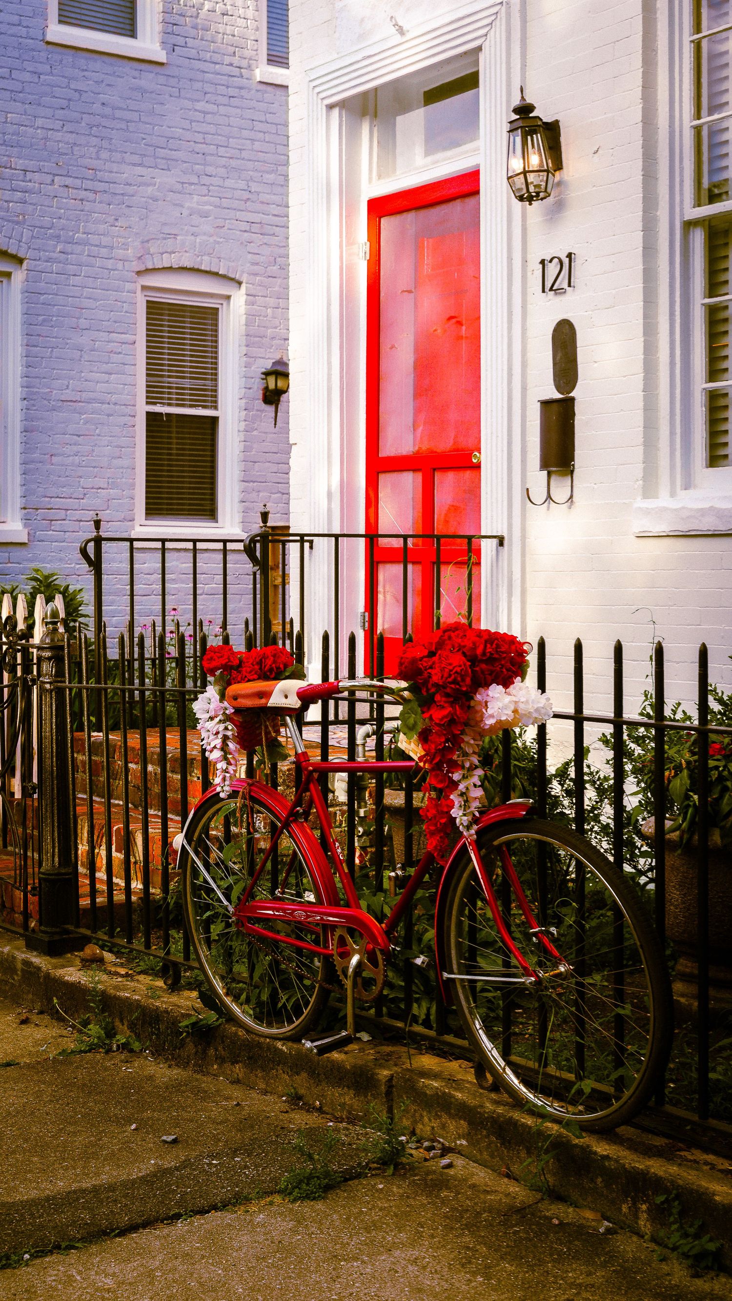 Red bicycles lean against white houses with matching red doors and black iron railings in a residential area.