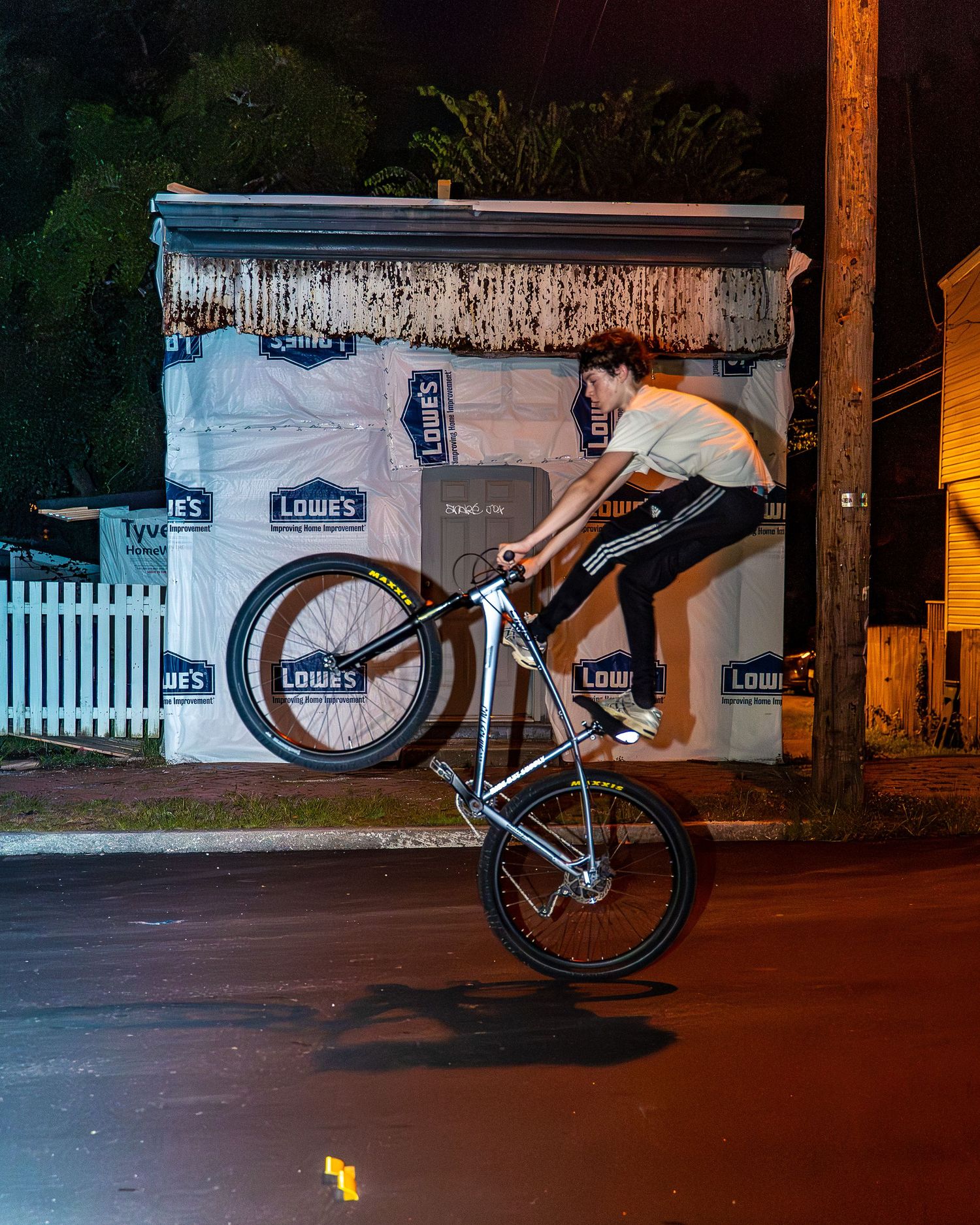 BMX rider executing trick maneuver at night near white picket fence.