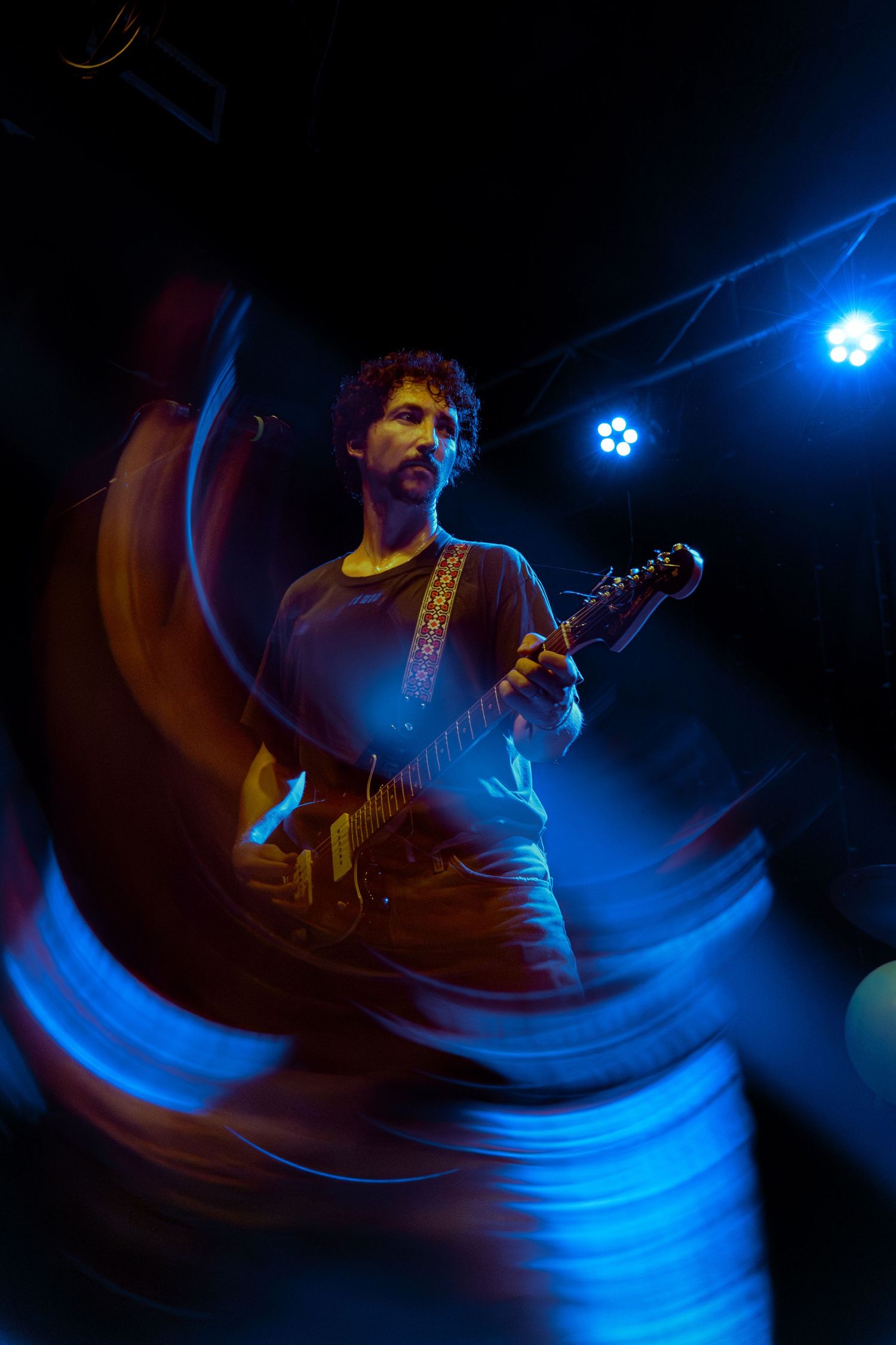 A guitarist performs on stage with dramatic blue lighting and motion blur effects creating an atmospheric concert scene.