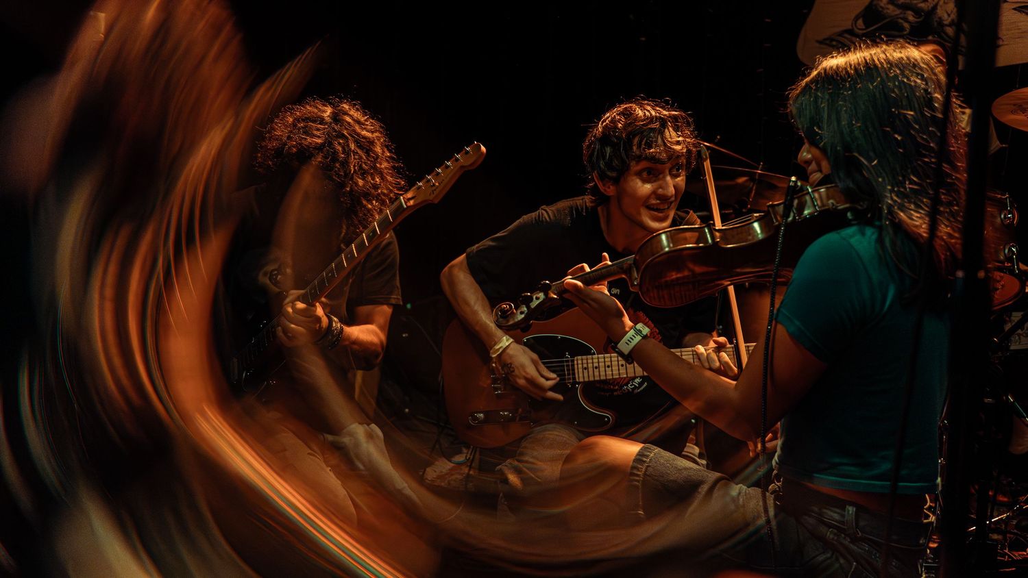 A string musician performs on stage in dark lighting with dramatic orange light streaks created by long exposure photography.