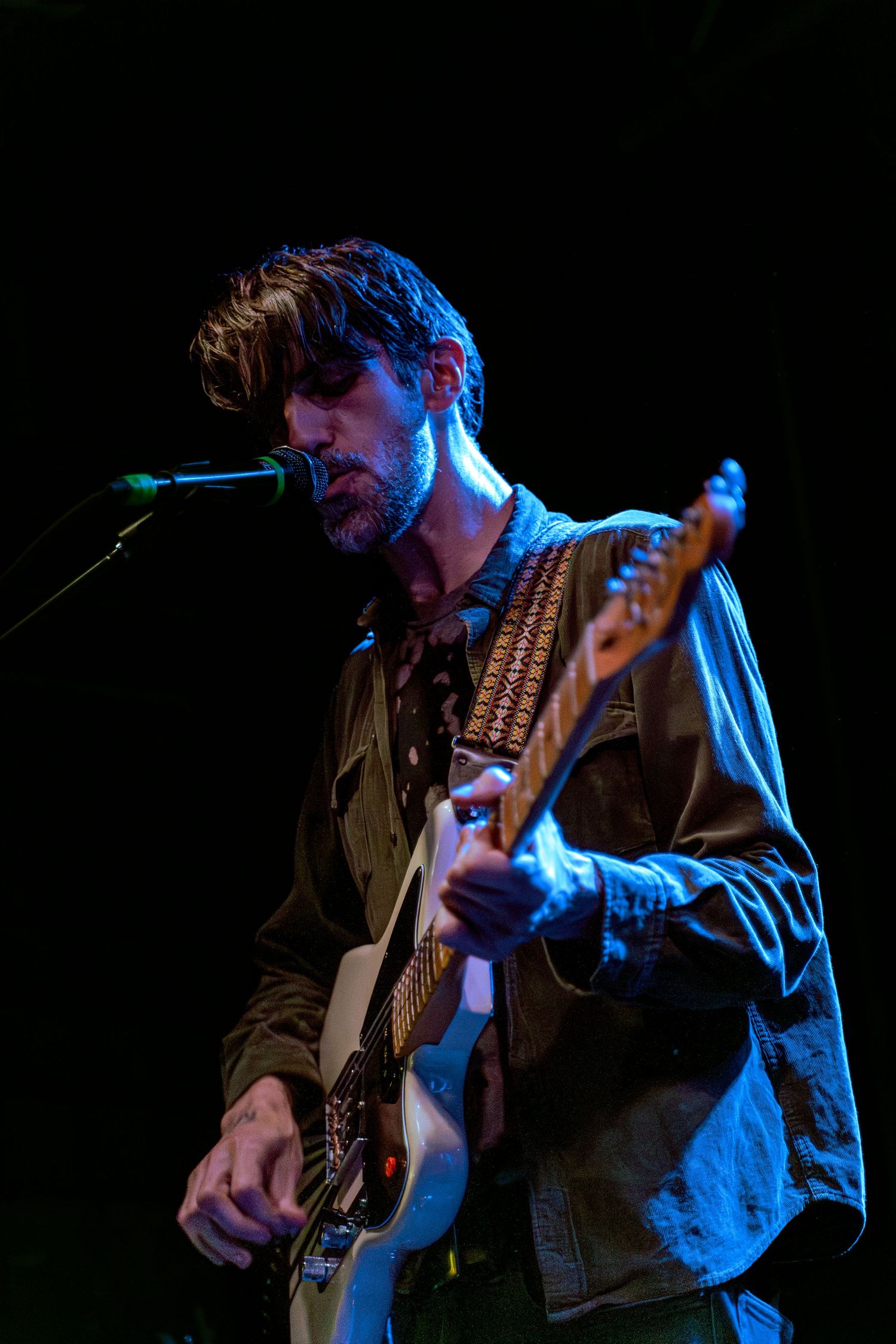 A musician plays a string instrument in a dramatic pose under blue stage lighting against a dark background.