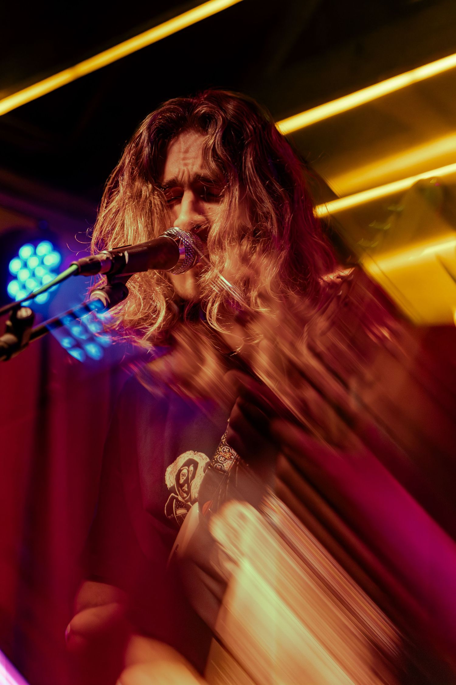 Motion blur captures a live performance with dramatic yellow stage lighting and red backdrop creating dynamic energy.