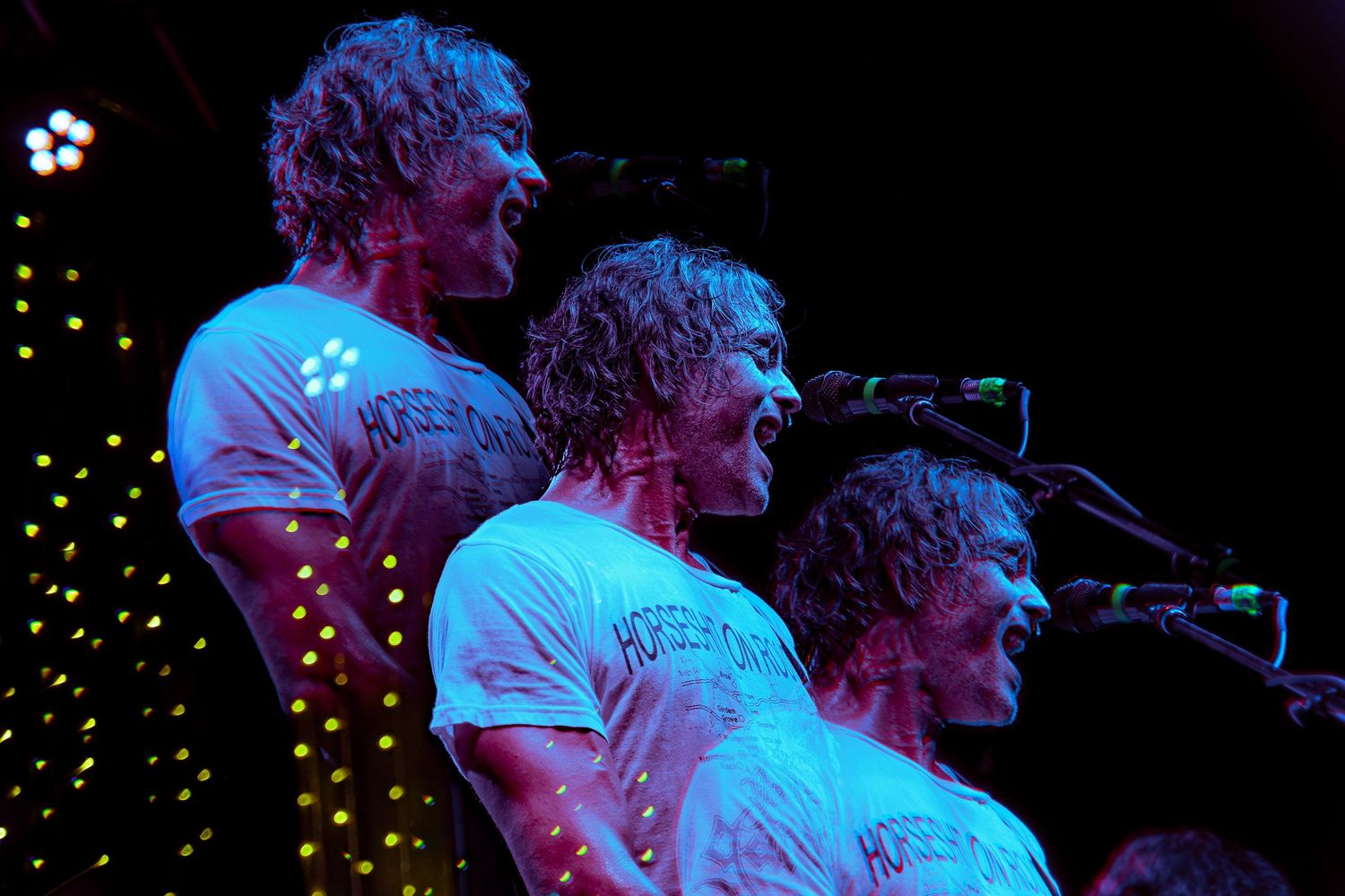 Musicians perform on stage under dramatic blue and pink lighting during a concert performance.