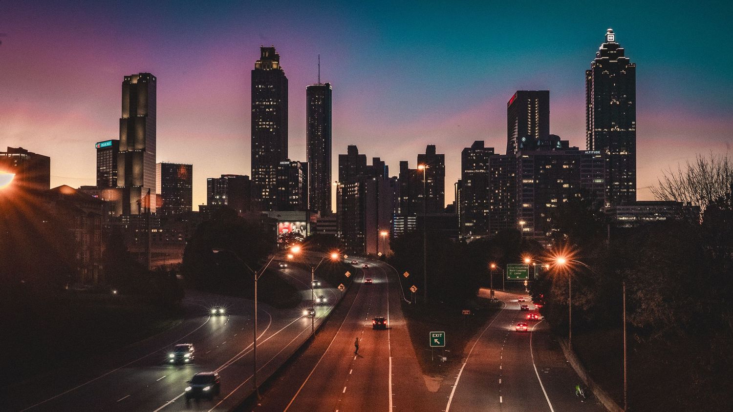 Dramatic sunset skyline of Atlanta with illuminated skyscrapers and highway in the foreground.