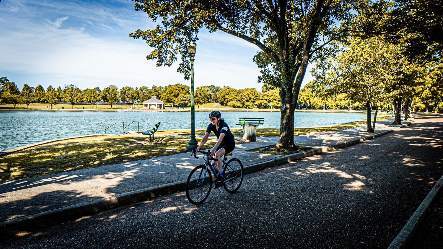 Cyclist rides along peaceful lakeside path with trees and water in background.