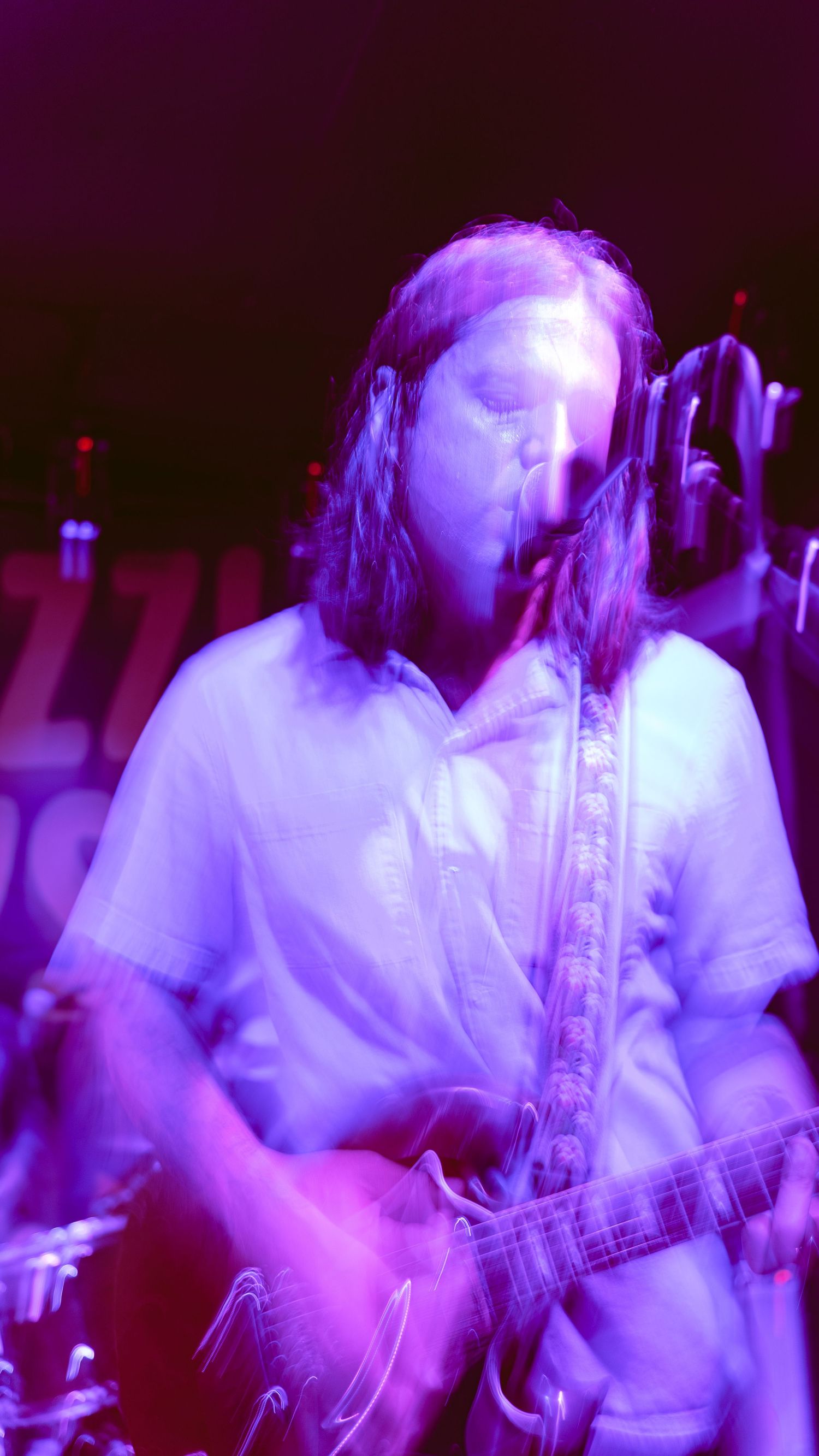 Multiple exposure shot of musician playing guitar under purple stage lights.