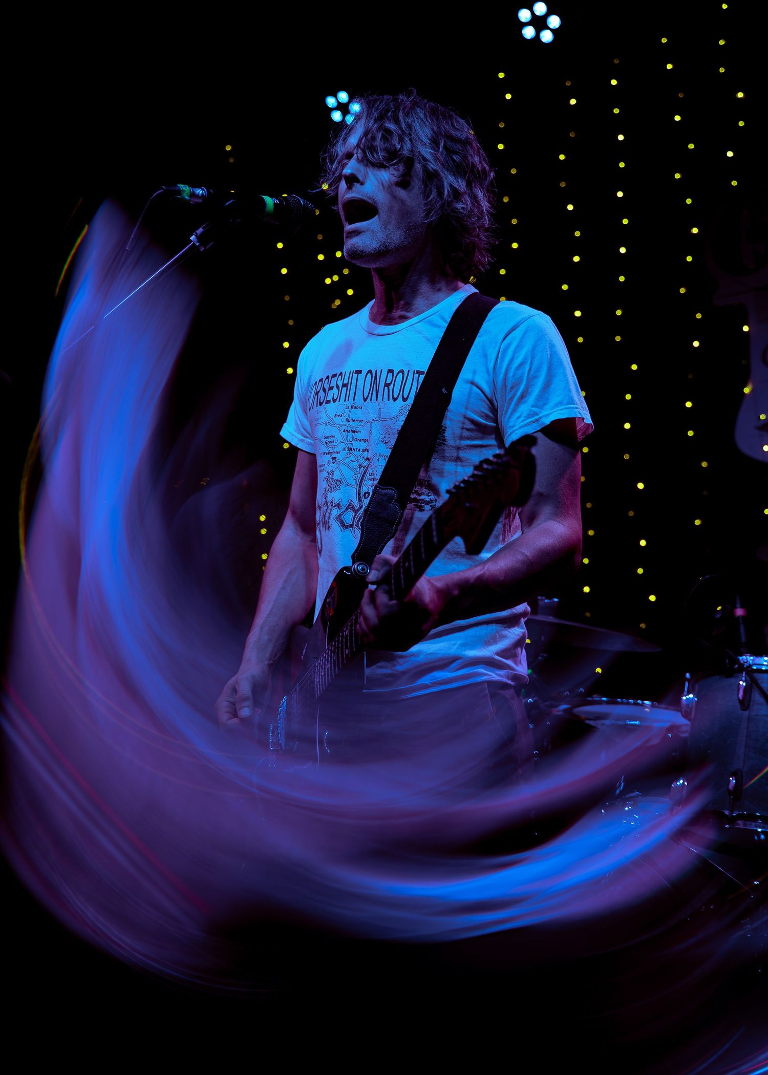 Concert performer illuminated by blue stage lights creates a dynamic motion blur effect against a starlit backdrop.