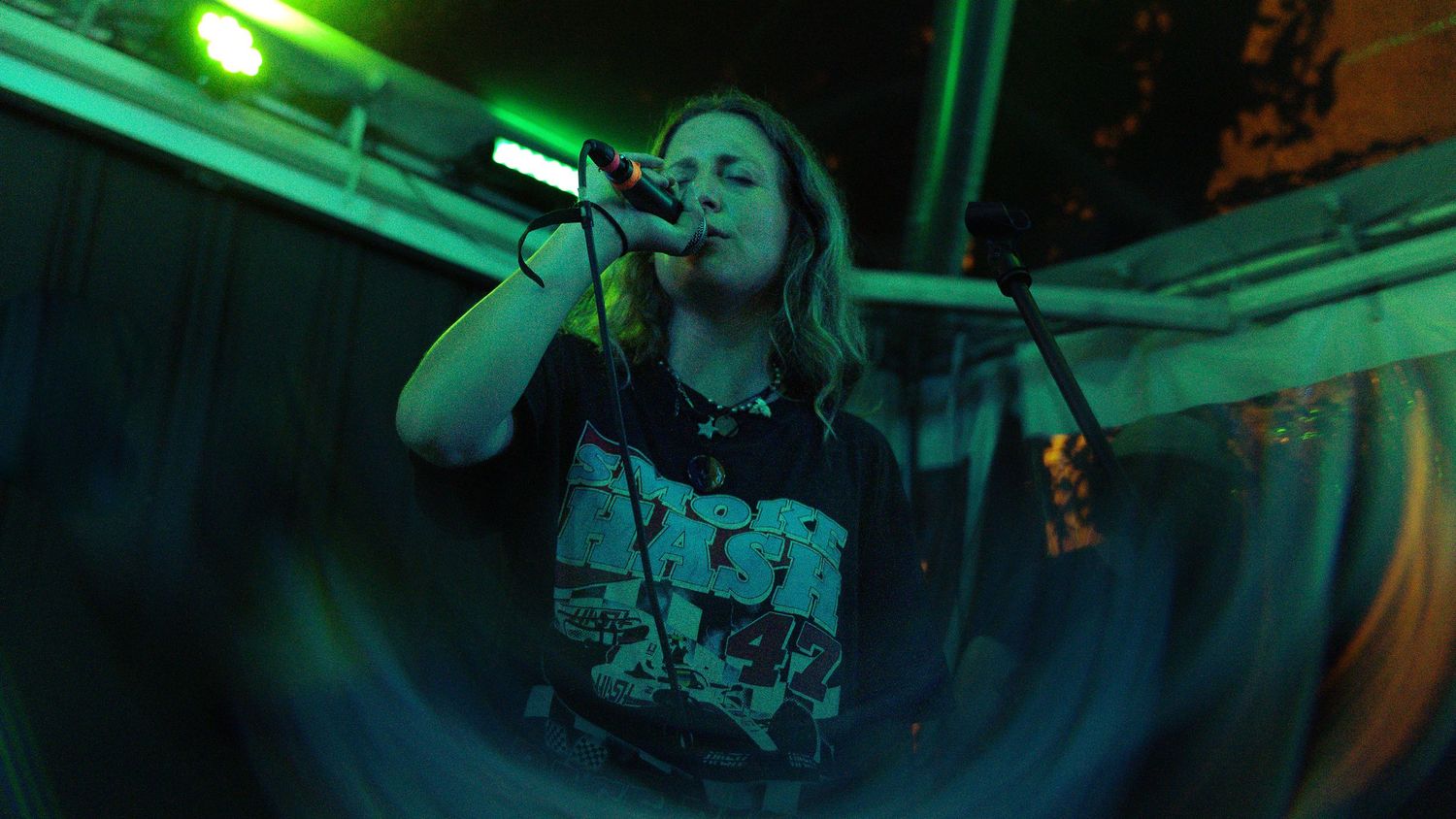 A performer sings on stage under green lighting at a concert venue.