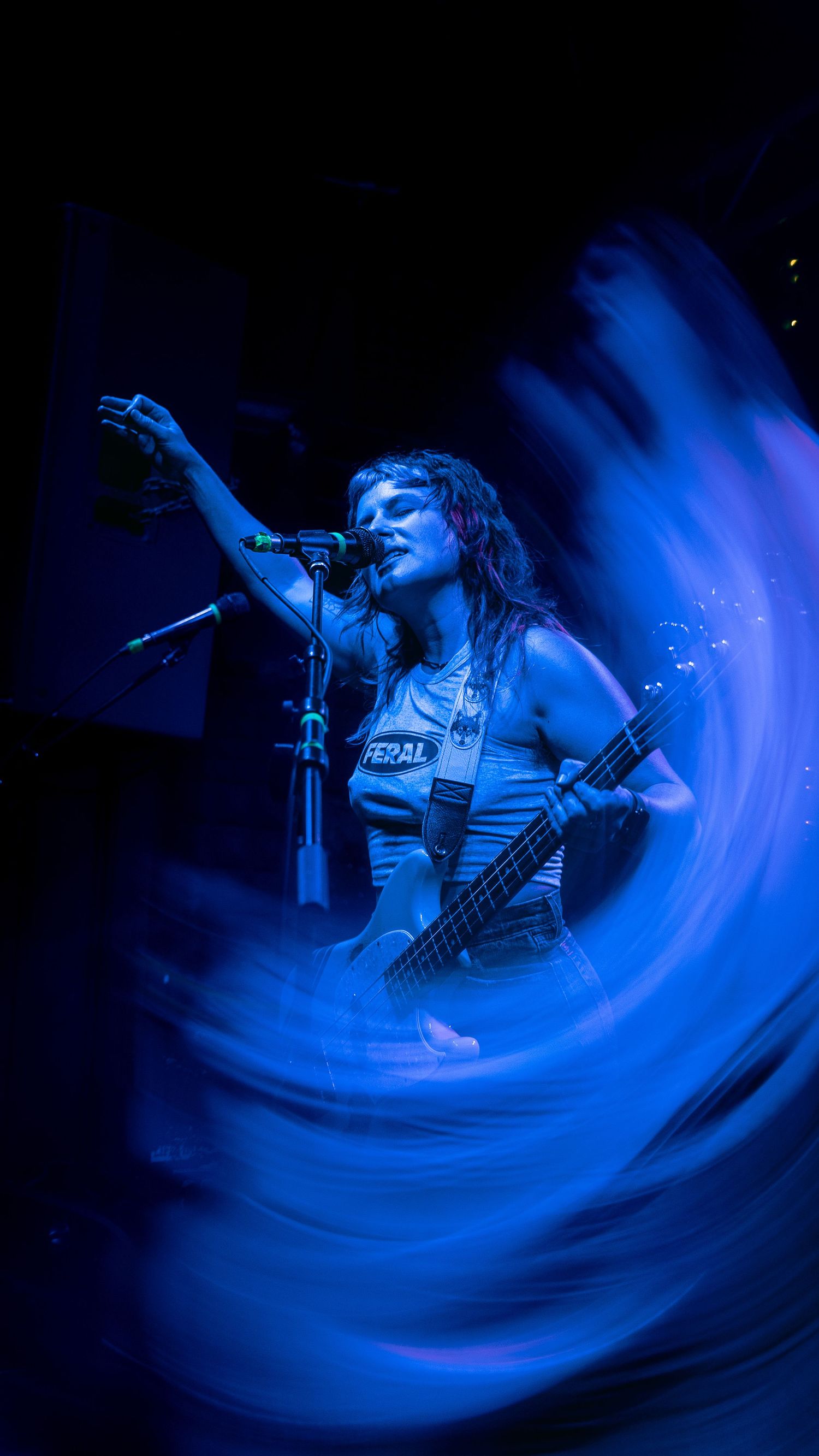 A vocalist performs on stage with dramatic blue swirling light effects creating a dynamic long exposure photograph.