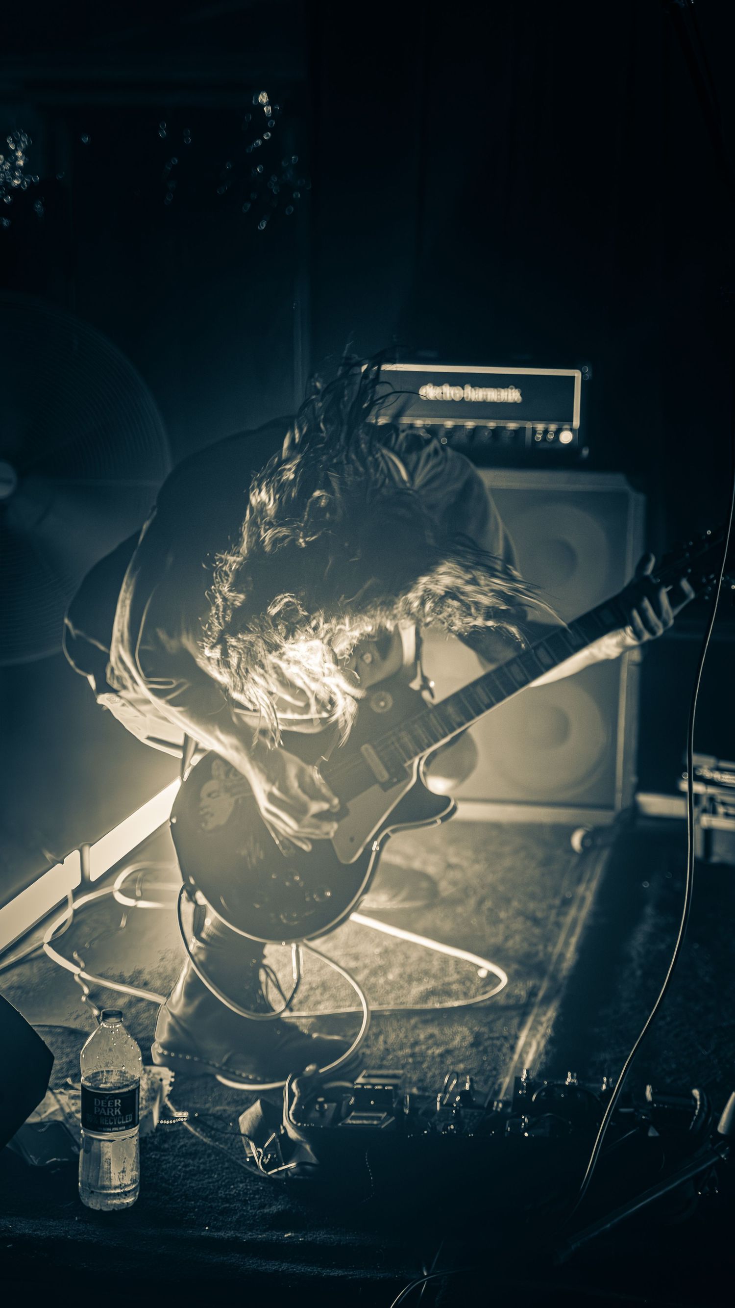 Monochrome concert photo showing performer with guitar against backlit stage setup.