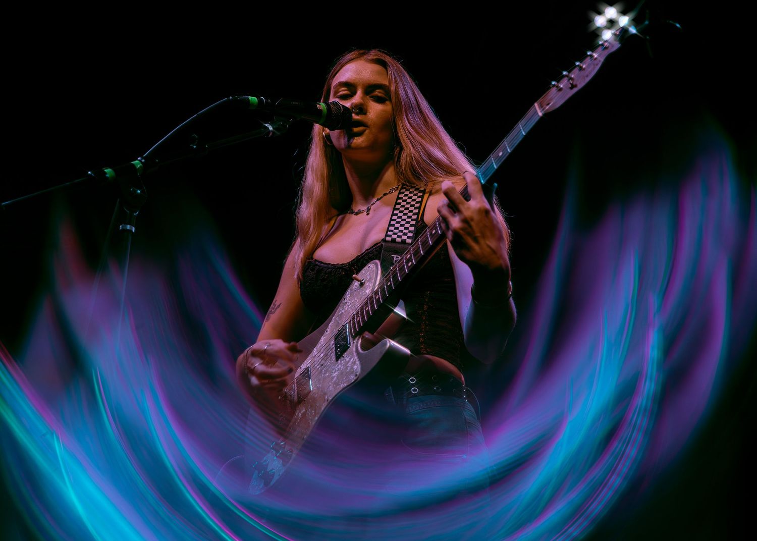 Dynamic concert photo with musician playing bass guitar against swirling blue and purple stage lighting effects.