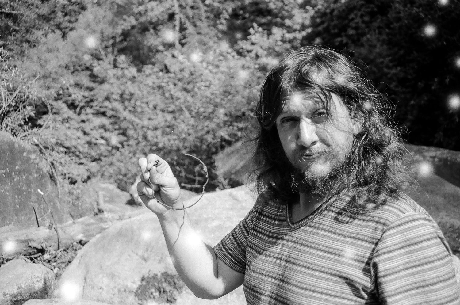 Black and white portrait of someone in a striped shirt holding something small outdoors.