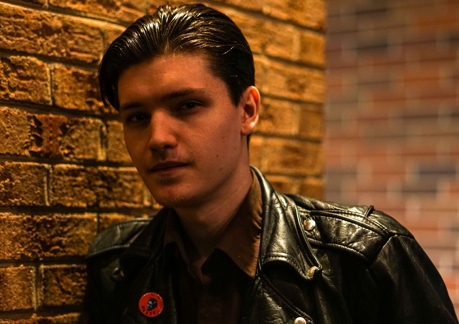 Moody portrait against brick wall with dramatic lighting and shadows.