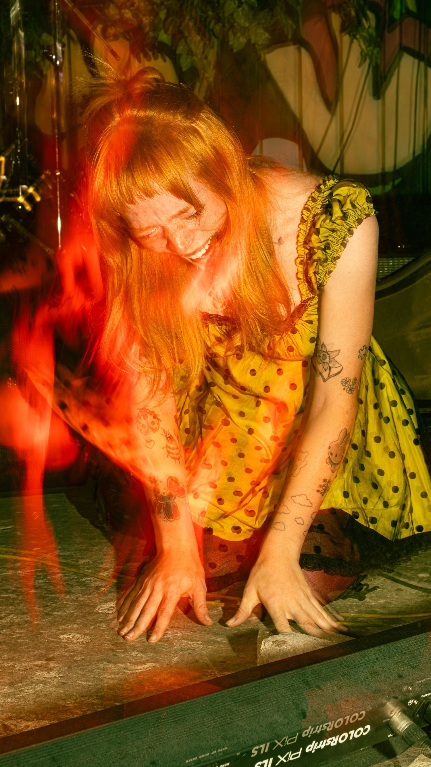 Performer in yellow dress smiling and bending down during energetic stage performance.