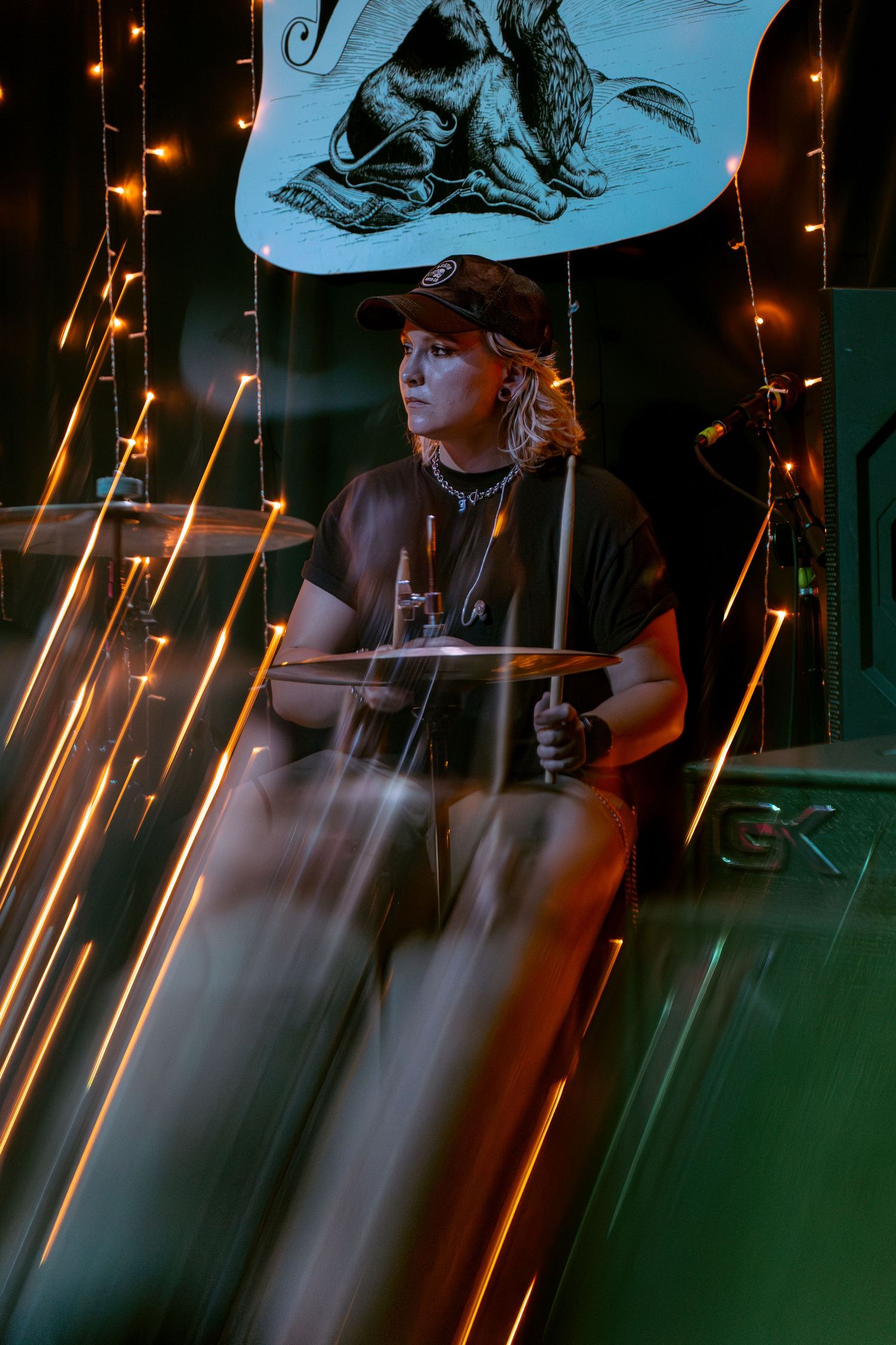 Person holds a flag while standing in front of sparkling light trails at night with a blue and green lighting aesthetic.