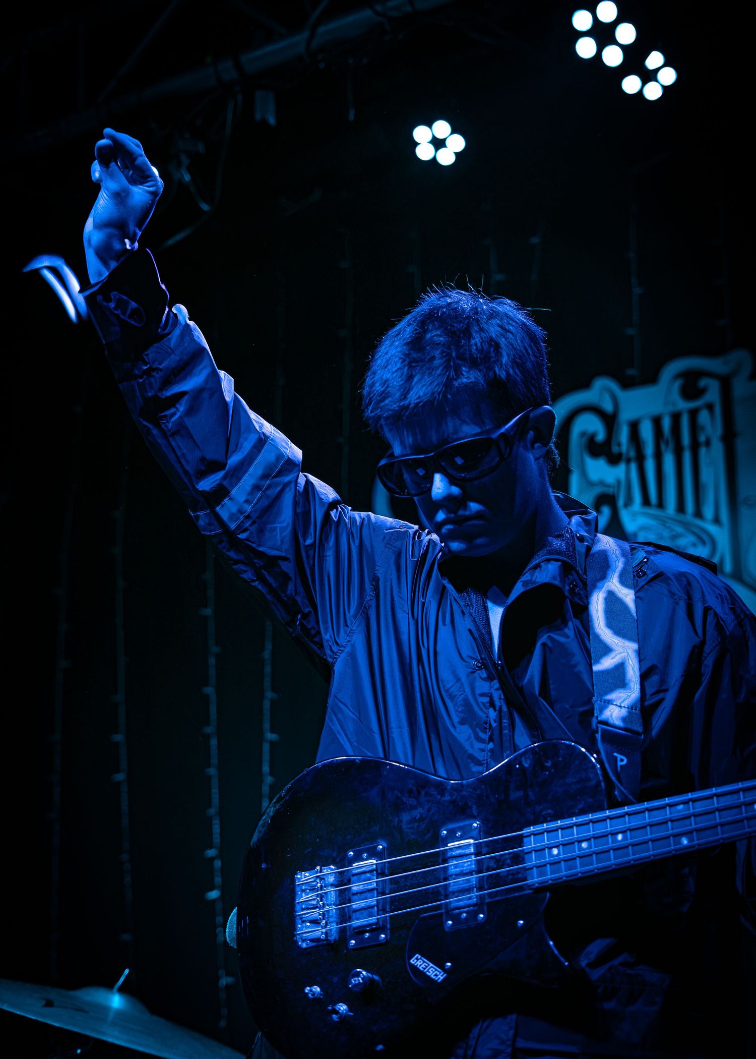 Musician playing bass guitar under blue stage lighting at a concert venue.