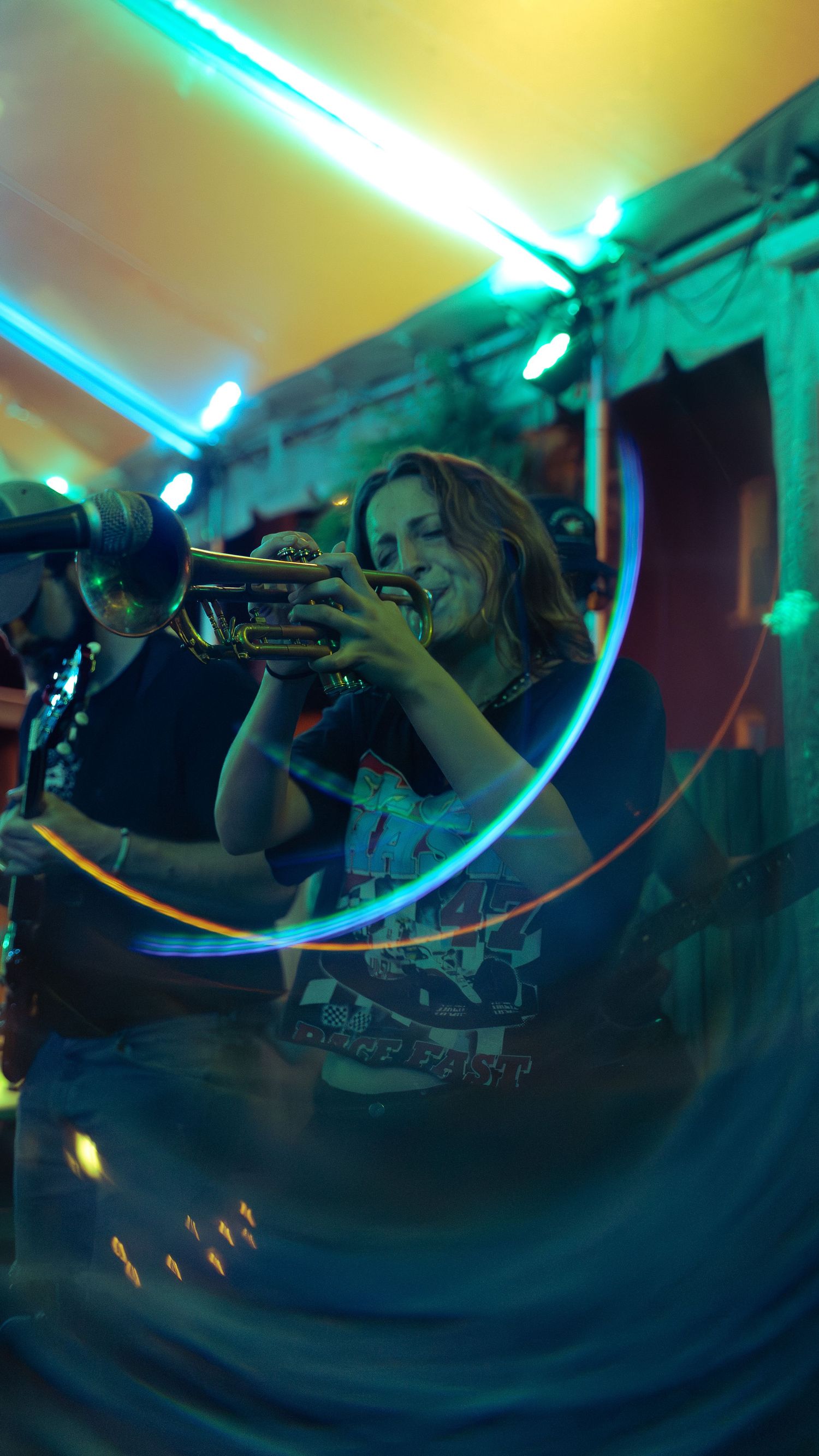 A row of musicians playing brass instruments under dramatic turquoise lighting during a nighttime performance.