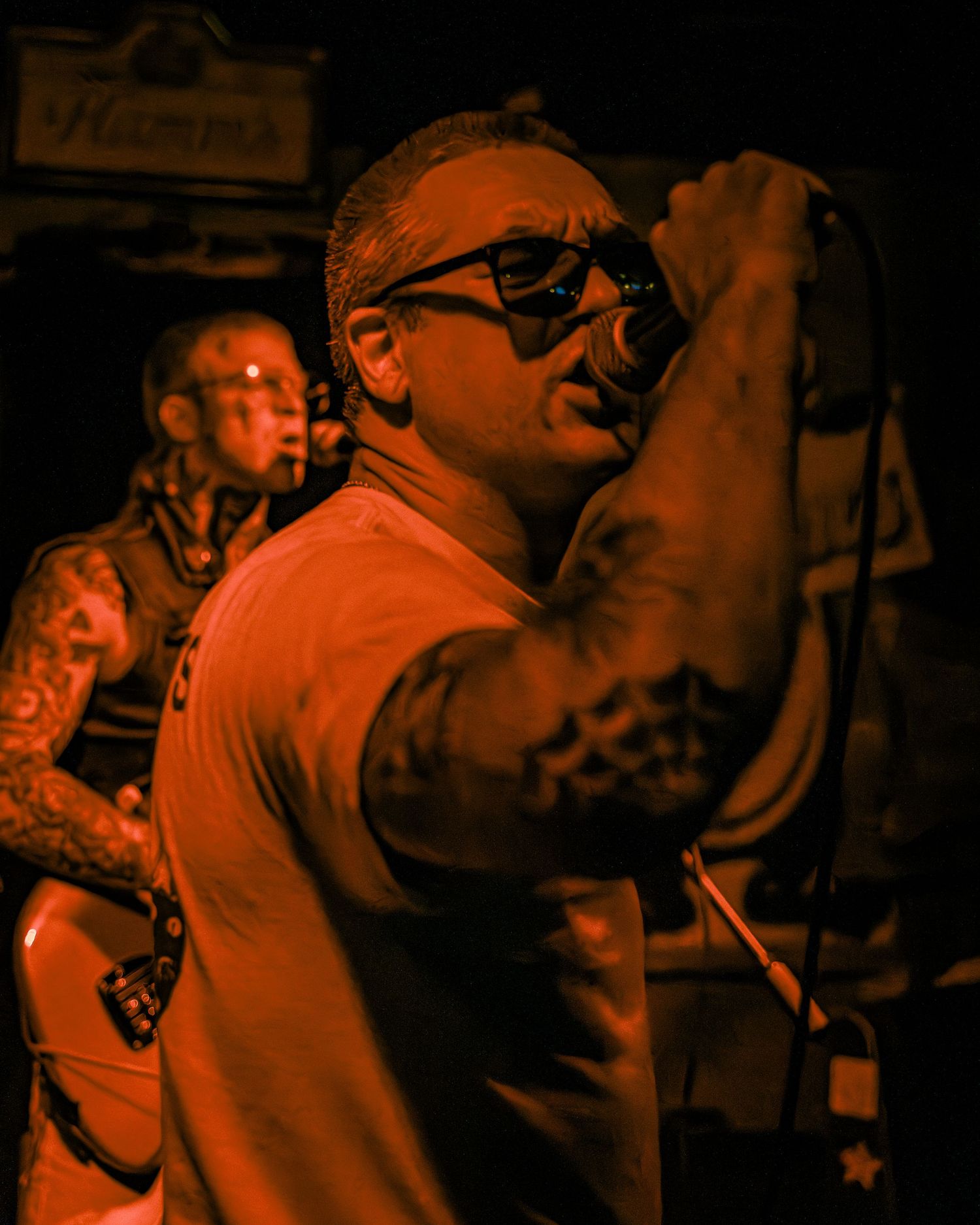 Lead singer performs passionately bathed in orange stage lighting while wearing glasses.