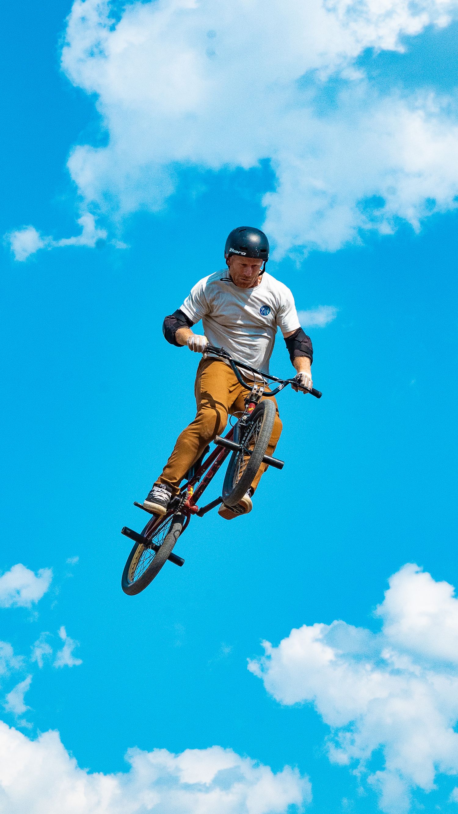 BMX rider tilts bike sideways during aerial maneuver with clouds in background.