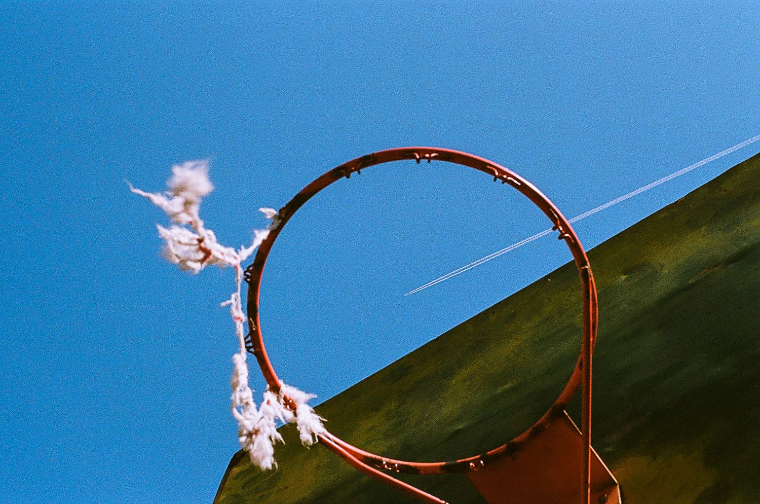 Basketball hoop rim against bright blue sky with white smoke or clouds trailing behind.
