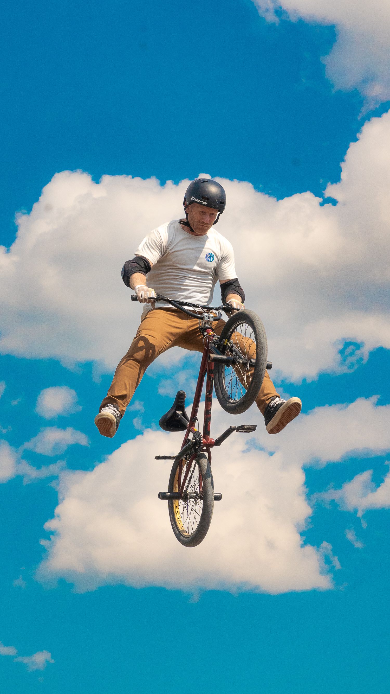 BMX rider performing aerial trick against blue sky with white fluffy clouds.