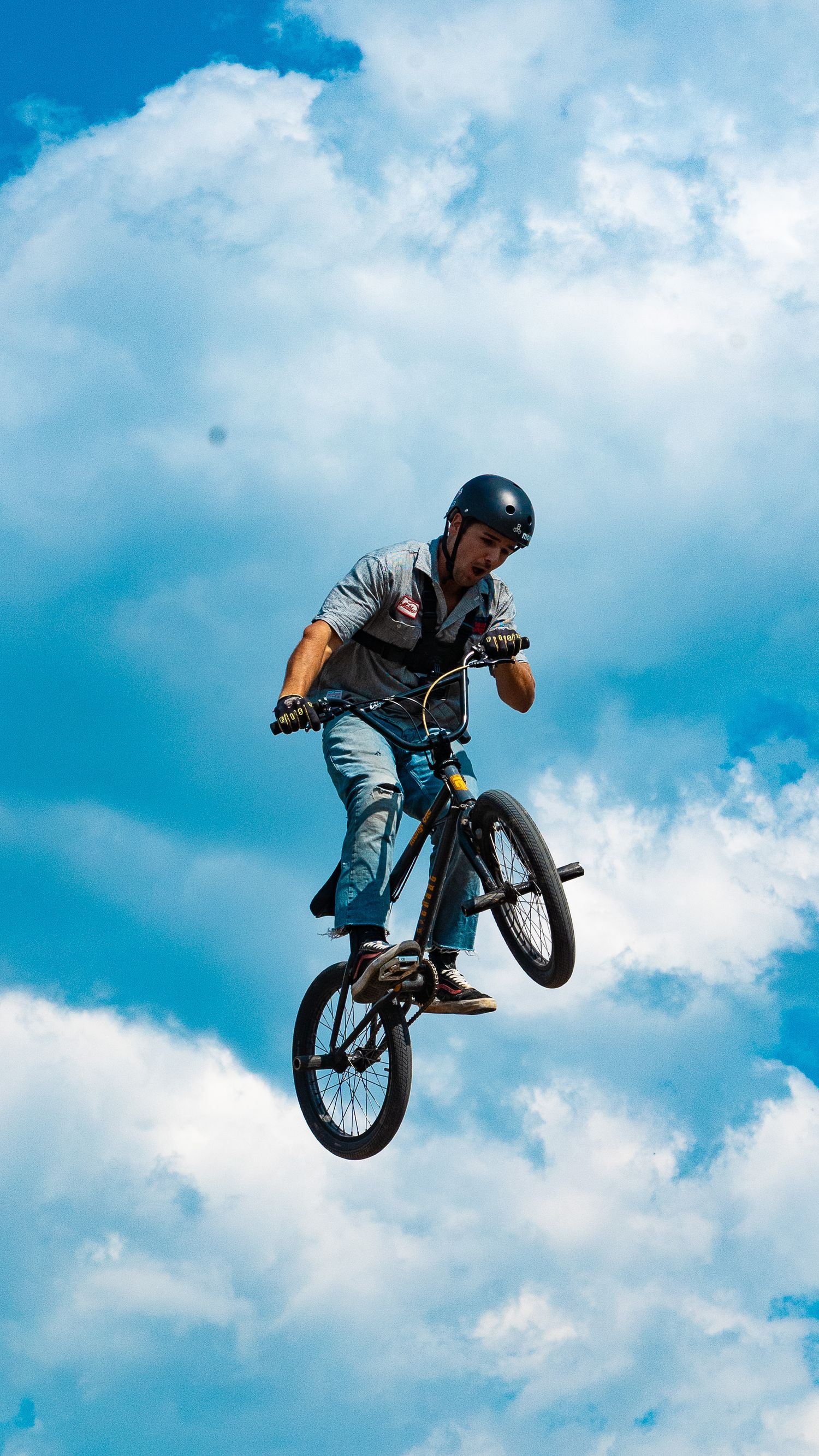 BMX rider performs a backflip trick against a blue sky with white clouds.