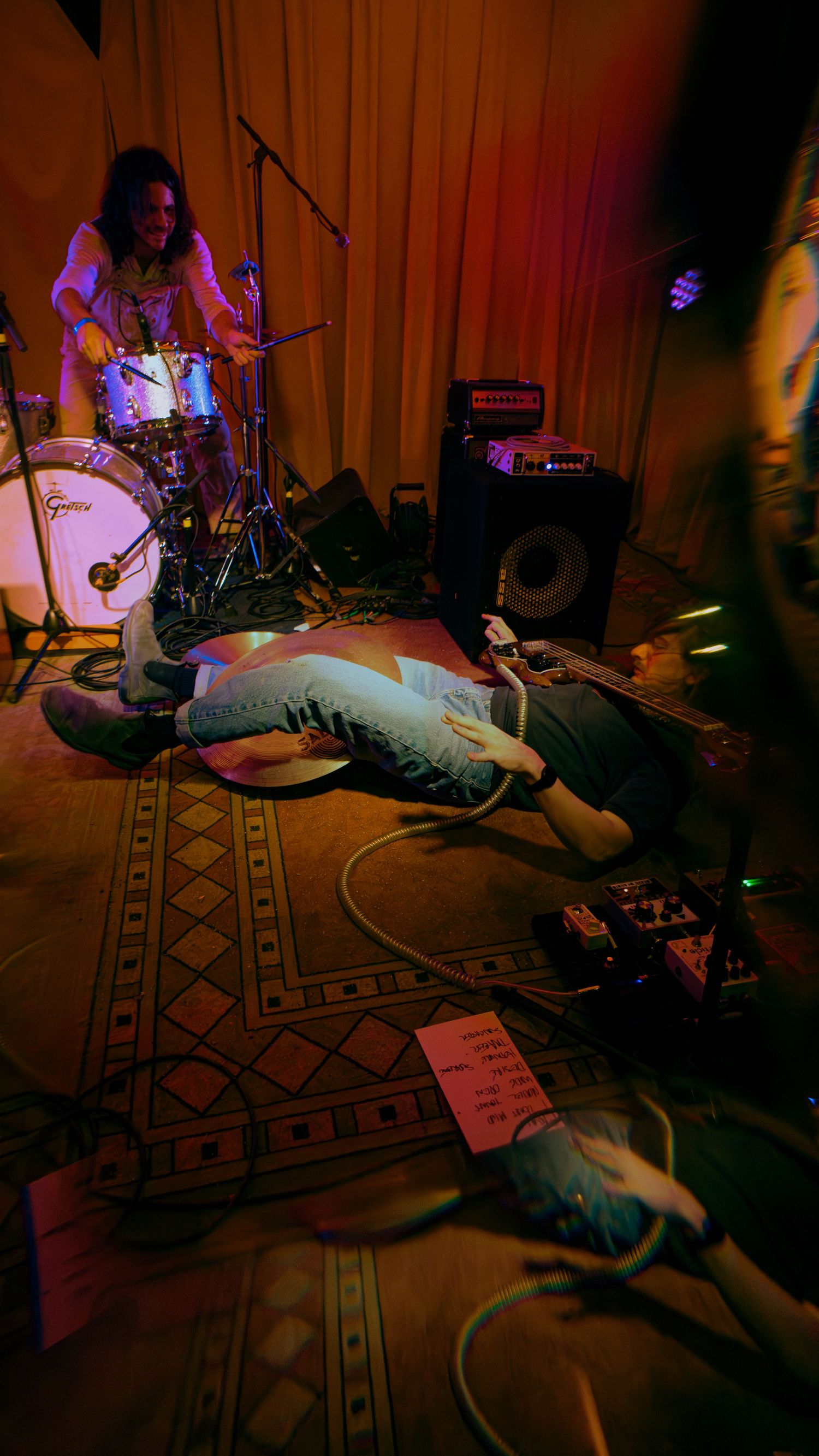 A sequence of dimly lit concert photos showing a performer lying on stage with an instrument in a warm orange light.