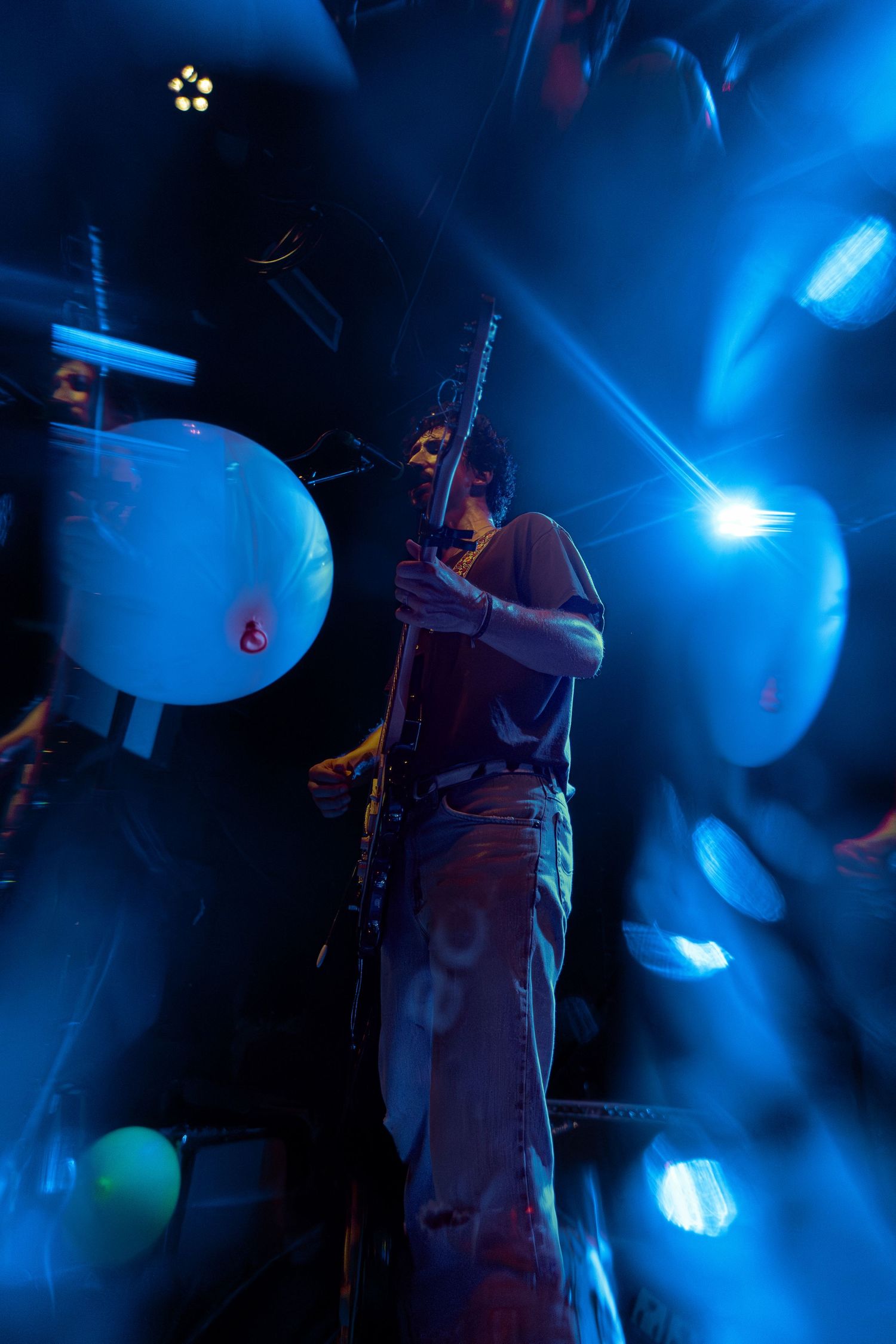Blue-tinted concert photo showing a drummer performing onstage with dramatic lighting effects and cymbals silhouetted.