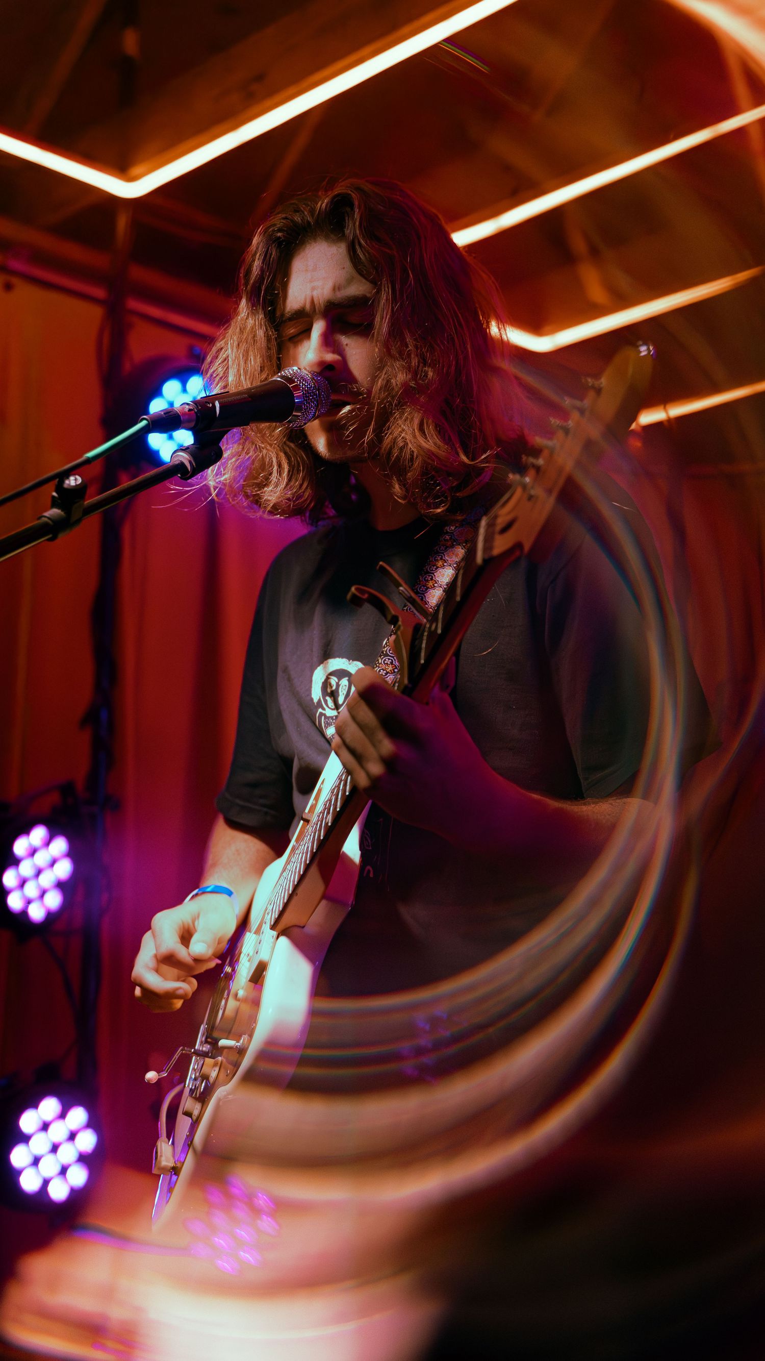 Musician performs with acoustic guitar on dimly lit stage under dynamic red and purple lighting effects.