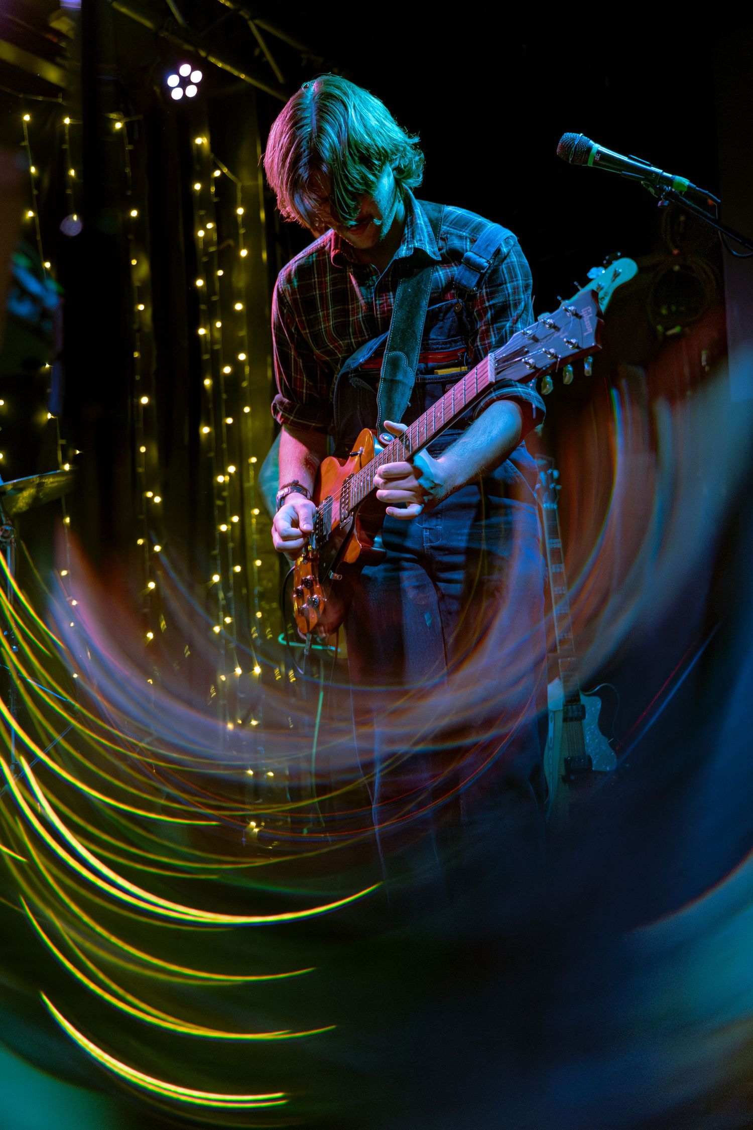 Musicians perform on stage with colorful blue lighting and yellow light trails creating dynamic motion effects.