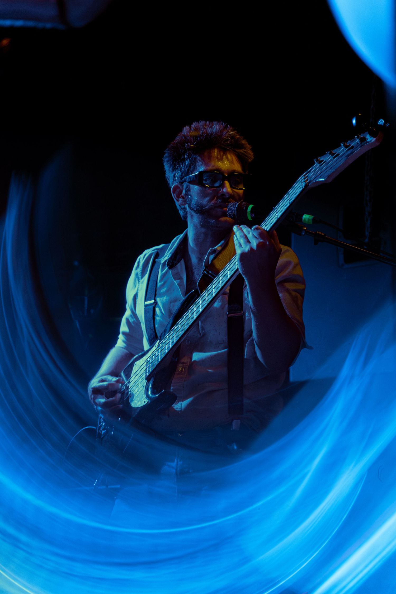 Multiple exposure photograph of a guitarist performing on stage with blue light trails creating dynamic motion effects.