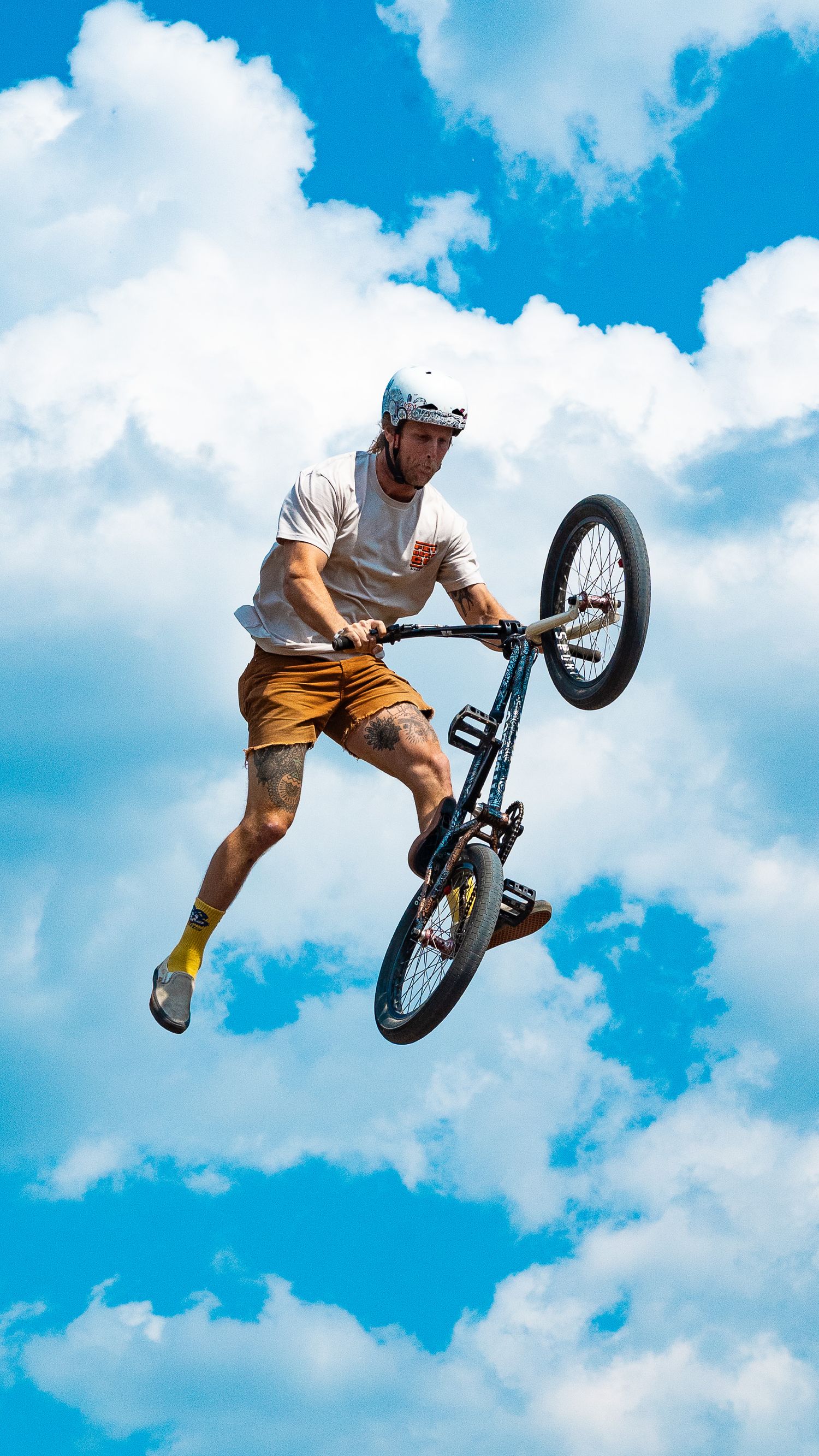 BMX rider performs aerial trick against bright blue sky with white clouds.