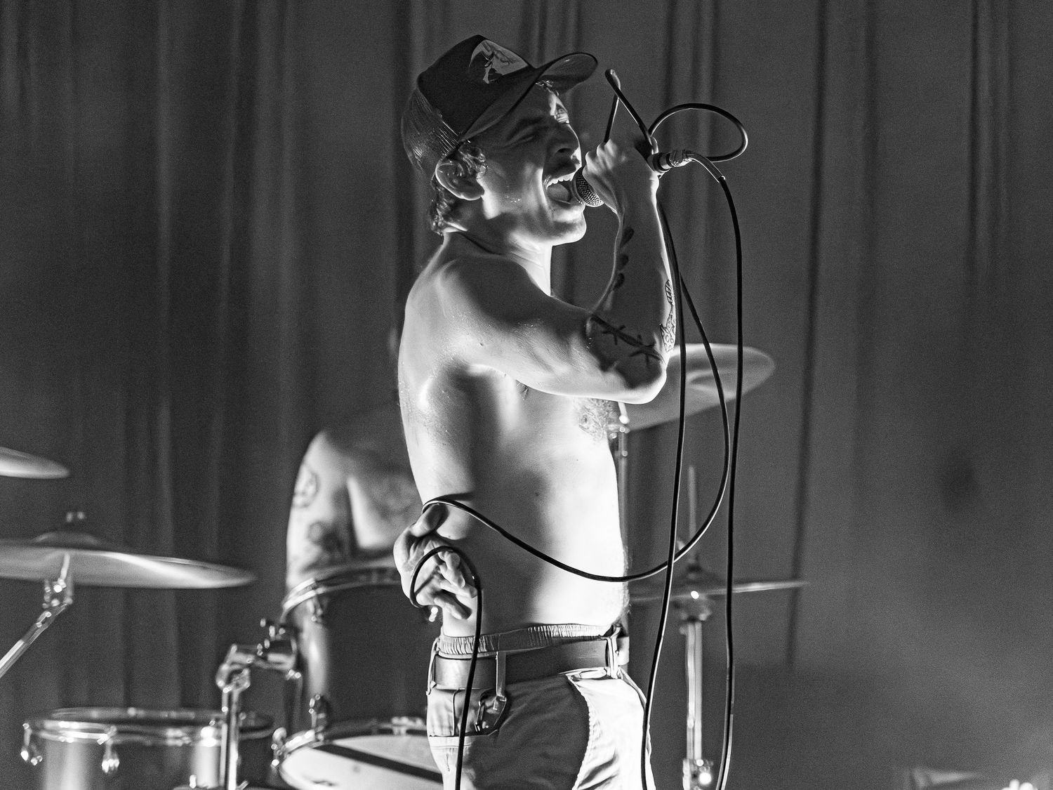 Black and white performance shot showing music equipment and stage setup.